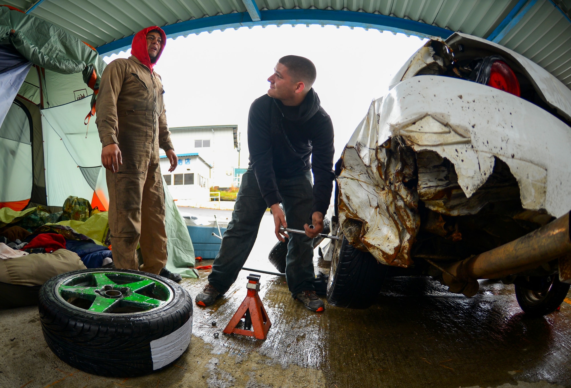Senior Airman Joseph Galloway, 730th Air Mobility Squadron jet propulsion technician, talks to Angelo Manalastes, a drift driver, while changing the tire on his drift car at Ebisu Circuit, Japan, Nov. 14, 2015. Drifting often burns tires down so quickly that they have to be changed at least twice a day, and causes such extensive damage that the cars cannot be legally driven outside the race track. (U.S. Air Force photo by Airman 1st Class Elizabeth Baker/Released)