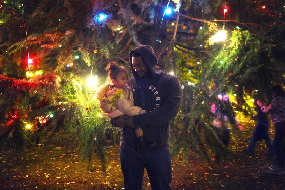 Staff Sgt. Andre Hayes, a 374th Civil Engineer Squadron journeyman, holds his daughter during the holiday tree lighting ceremony at Yokota Air Base, Japan, Nov. 24, 2015. The lighting of the tree signals the beginning of the holiday season. (U.S. Air Force photo/Airman 1st Class Delano Scott)