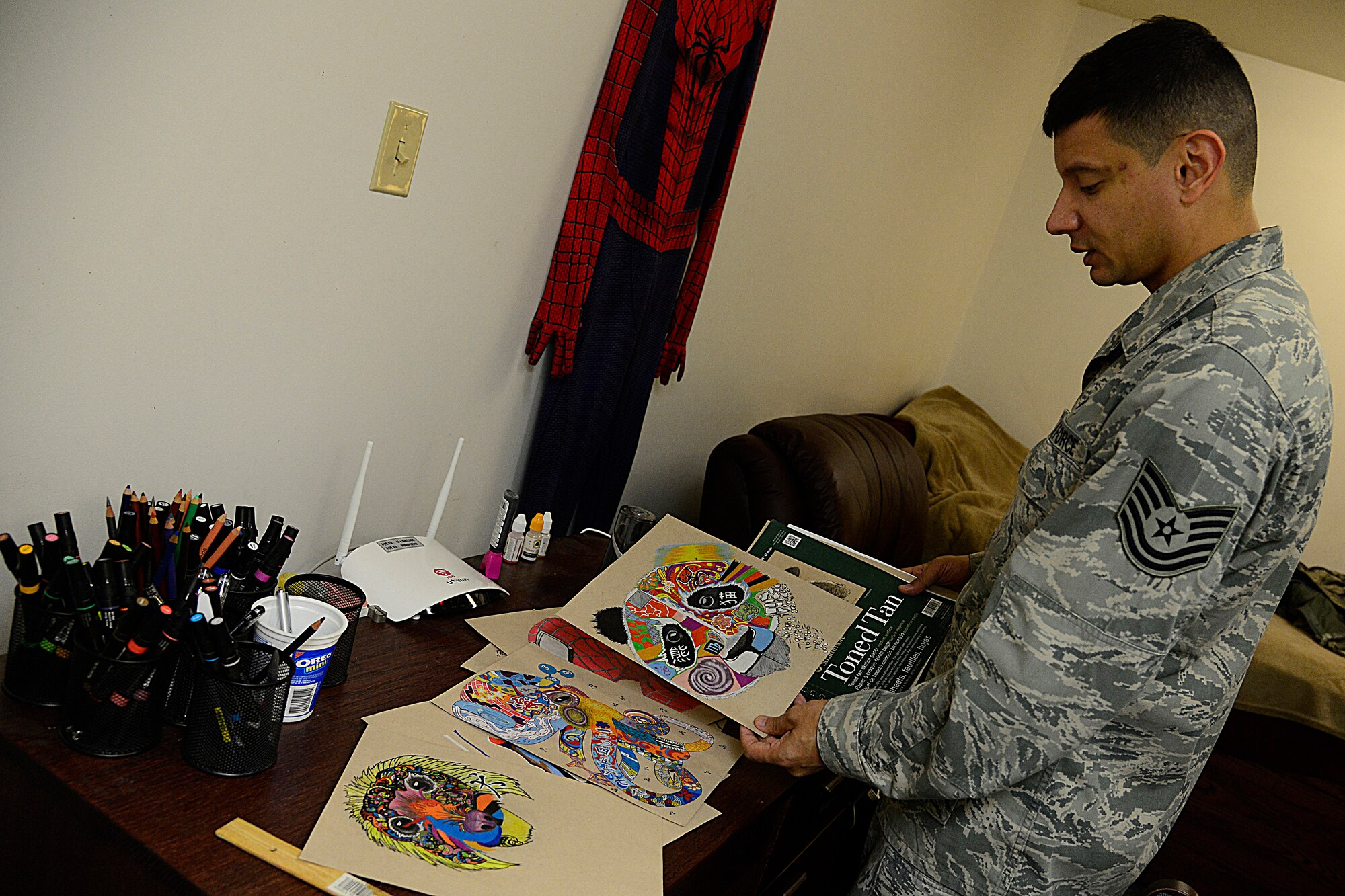 Tech. Sgt. Juan Hernandez, 731st Air Mobility Squadron air terminal operations center senior information controller, shows various artworks on Osan Air Base, Republic of Korea, Dec. 3, 2015. Hernandez learned early on that he could not see many colors on the electromagnetic spectrum that are visible to the human eye, but prevailed in learning how to draw detailed and vibrant works of art. Through dedication, he taught himself to read colors based off of name or issued number. (U.S. Air Force photo/Senior Airman Kristin High)