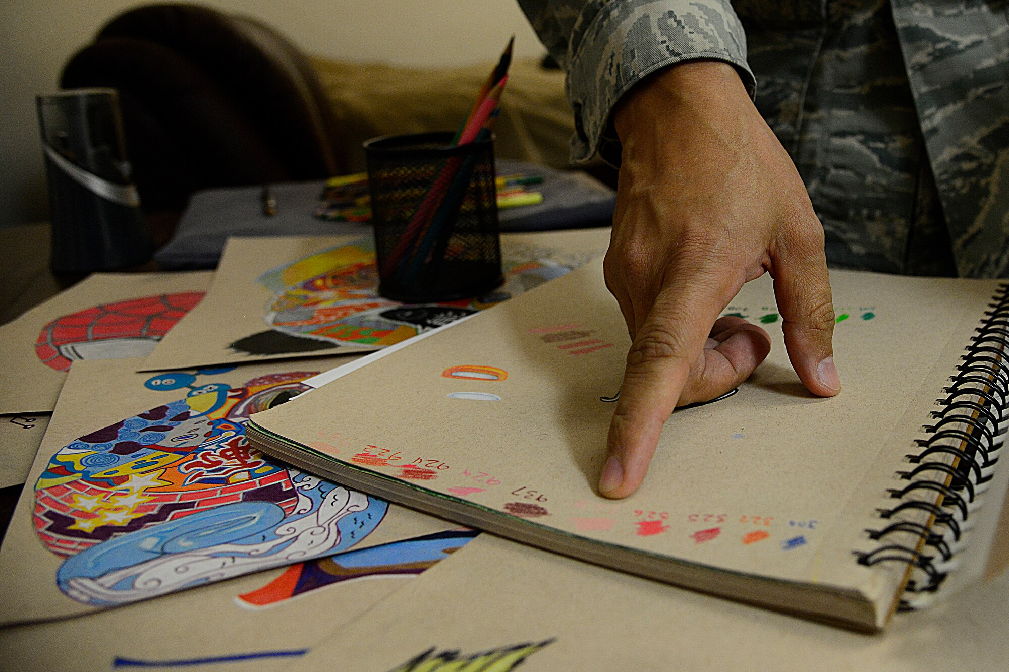 Tech. Sgt. Juan Hernandez, 731st Air Mobility Squadron air terminal operations center senior information controller, shows his coloring system on Osan Air Base, Republic of Korea, Dec. 3, 2015. Hernandez learned early on that he could not see many colors on the electromagnetic spectrum that are visible to the human eye, but prevailed in learning how to draw detailed and vibrant works of art. Hernandez taught himself to read colors based off of name or issued number and creates sample pages to make sure his artwork is accurately portrayed. (U.S. Air Force photo/Senior Airman Kristin High)