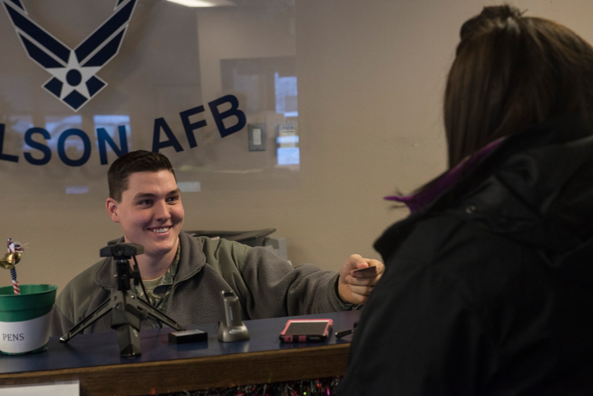 U.S. Air Force Airman 1st Class Seth Nolte, a 354th Security Forces Squadron Defender in the pass and registration section, helps a customer in the Visitor Control Center on Dec. 2, 2015, at Eielson Air Force Base, Alaska. Nolte said he enjoys helping and interacting with the community along with providing assistance to the public. (U.S. Air Force photo by Staff Sgt. Joshua Turner/Released)