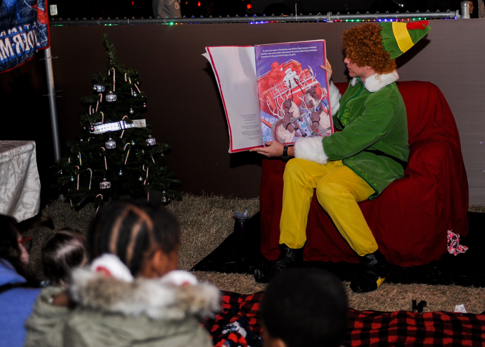 Buddy the elf reads a story to children during the Starry, Snowy, Southwest Night event at Davis-Monthan Air Force Base, Ariz., Dec. 3, 2015. Volunteers organized festivities that included photos with Santa, story time with Buddy the Elf, a mechanical snowboard and 60 tons of snow. (U.S. Air Force photo by Airman Basic Nathan H. Barbour/Released)