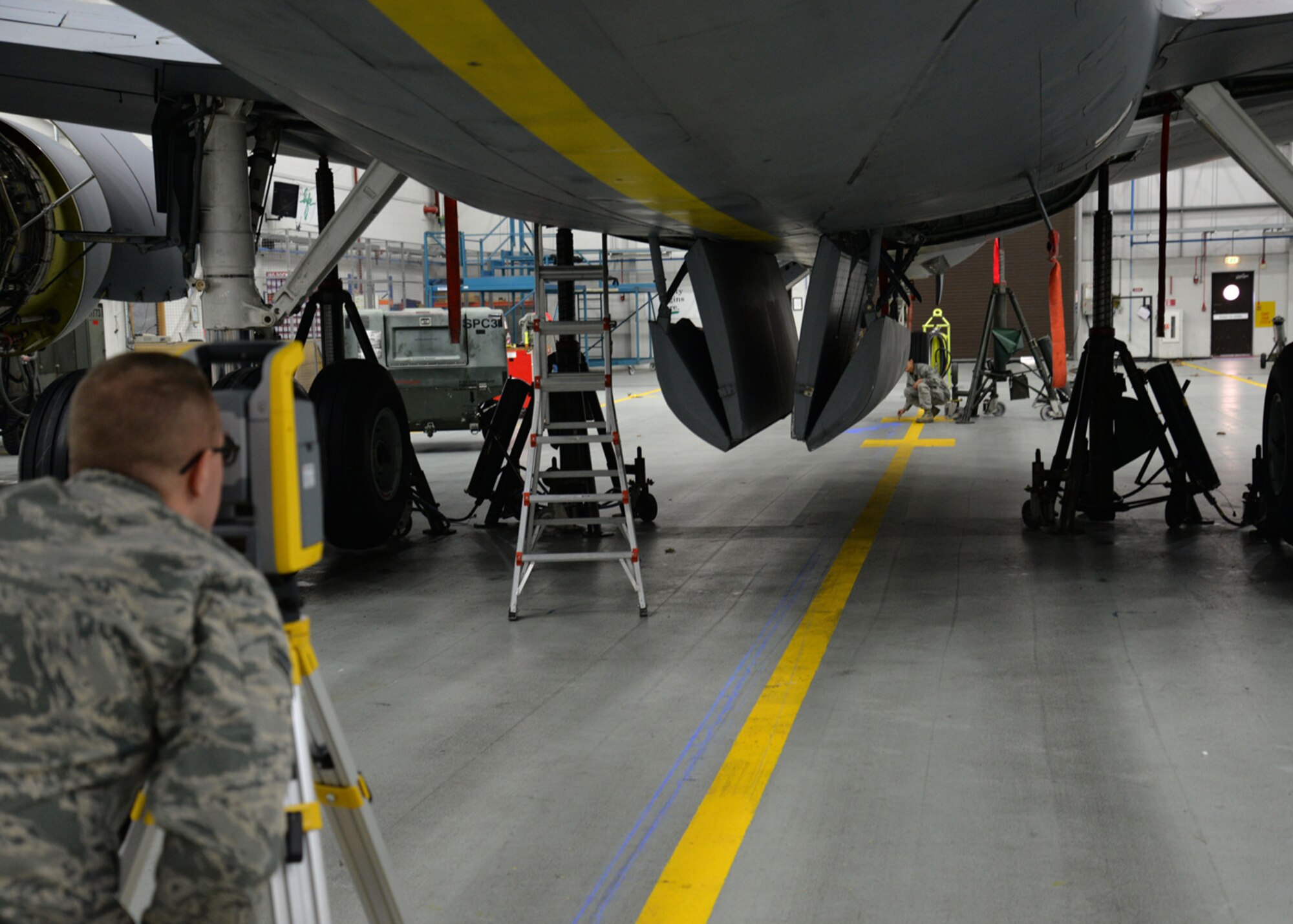 U.S. Air Force Airman 1st Class Brandon Adams, left, 100th Civil Engineer Squadron engineering flight journeyman, uses a geodimeter to take measurements as U.S. Air Force Senior Airman Abigail slater, also a 100th CES engineering flight journeyman, marks a precise spot underneath a KC-135 Stratotanker Nov. 23, 2015, on RAF Mildenhall, England. A plumb bob was initially used to mark exact vertical points around the aircraft, before three sets of measurements were taken to get the average and compile data. The 100th CES Airmen performed an alignment check to search for any shift in alignment which could damage the aircraft. (U.S. Air Force photo by Karen Abeyasekere/Released)