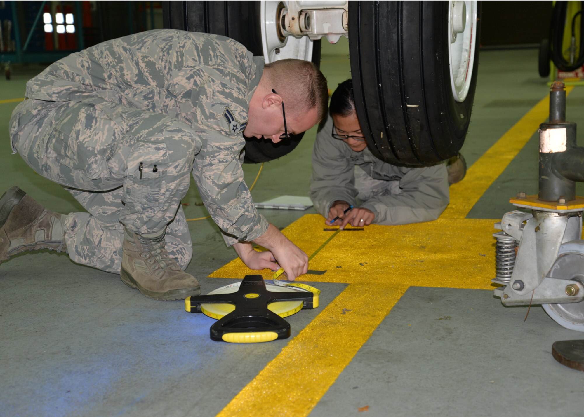 U.S. Air Force Airman 1st Class Brandon Adams, left, and U.S. Air Force Senior Airman Abigail Slater, both 100th Civil Engineer Squadron engineering flight journeymen, take measurements from specific points marked underneath a KC-135 Stratotanker Nov. 23, 2015, on RAF Mildenhall, England. The 100th CES Airmen were performing an alignment check on the jet to search for any shift in alignment. Three sets of measurements were taken to find the average, before compiling the data for the 100th Aircraft Maintenance Squadron. (U.S. Air Force photo by Karen Abeyasekere/Released)