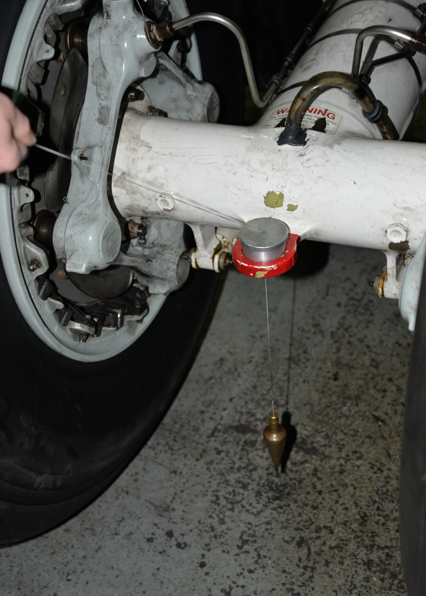 A plumb bob is hung through a tow ring between a set of aircraft wheels to determine an exact vertical point as part of measurements taken for an alignment check on a KC-135 Stratotanker Nov. 23, 2015, on RAF Mildenhall, England. Airmen from the 100th CES performed an alignment check on the aircraft following a hard landing recently. This is only the third time in six years that this check has been performed at RAF Mildenhall. (U.S. Air Force photo by Karen Abeyasekere/Released) 