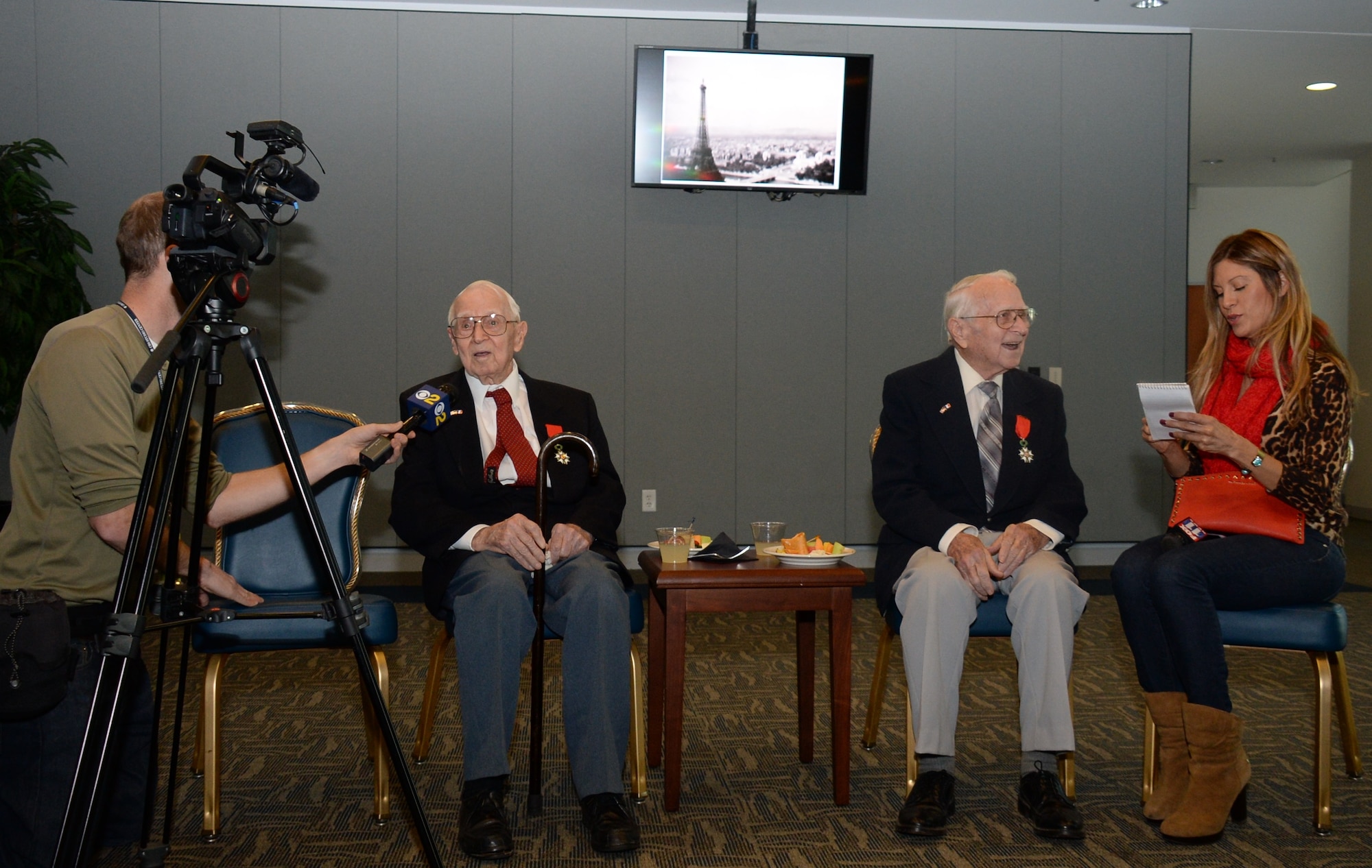 Retired Air Force Reserve Majs. Raymond “Glenn” Clanin and Russell “Lynn” Clanin take time for interviews with reporters from various Los Angeles television stations in the Gordon Conference Center at the Schriever Space Complex of the Space and Missile Systems Center at Los Angeles Air Force Base in El Segundo, Calif., Dec. 2. The 92-year-old twin brothers are recent recipients of the French government's highest distinction for their military service as World War II veterans, the Legion of Honor medal, presented by Christophe Lemoine, French consul general in Los Angeles. In the background is an aerial photo of the Eiffel Tower, taken from the right pilot’s seat of the B-26 Marauder named Flak-Bait by Maj. Glenn Clanin as he “buzzed” the famous landmark after the Liberation of France during WWII. (U.S. Air Force photo/Van De Ha)