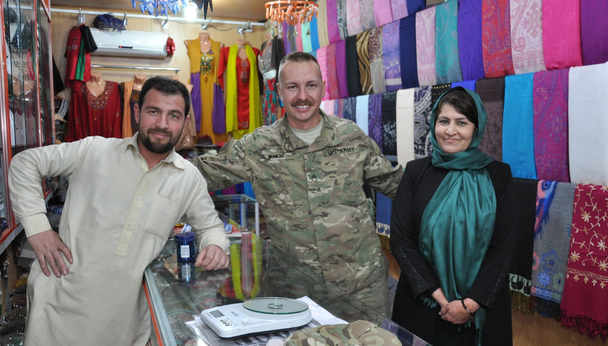 U.S. Army Staff Sgt. Matthew Amon and project managers of a local orphanage in Kabul, Afghanistan, pose for a photo at a store in the base bazaar. Amon, a security forces squad leader at Train, Advise, Assist Command-Air (TAAC-Air), met the couple and helped set-up a school supply drive with family and friends back home in Texas to donate to children at a local orphanage.  Amon is deployed from the 442nd Engineer Company as part of the Texas Army National Guard.  (U.S. Air Force photo by Capt. Eydie Sakura/released)