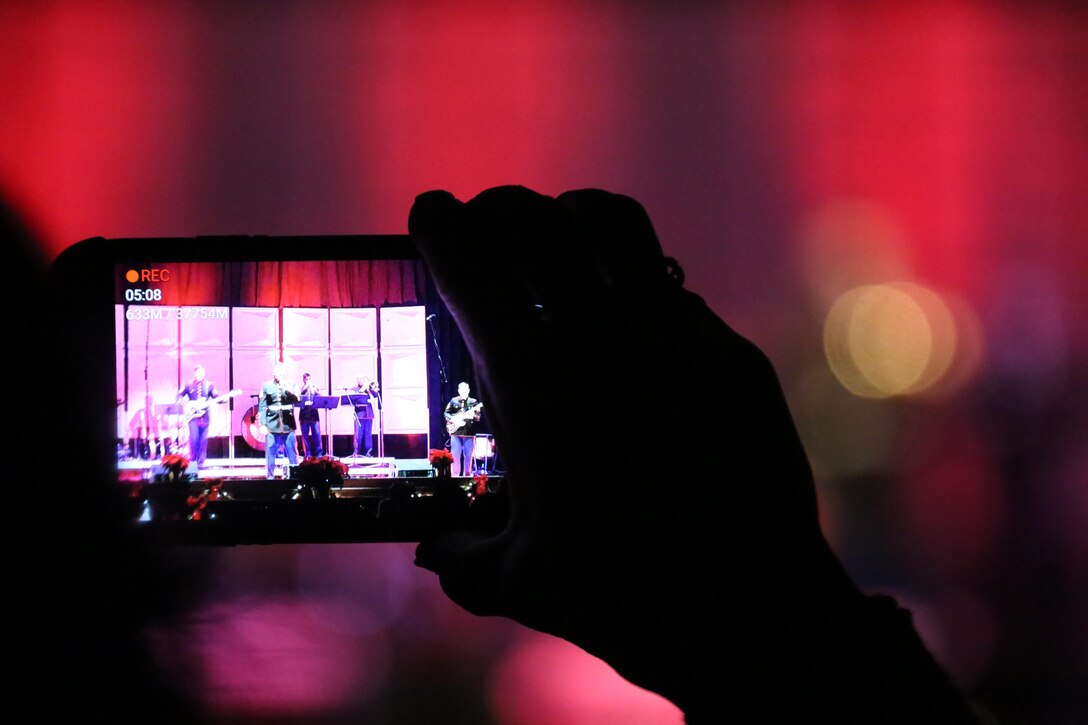 An audience member records the members of the 2nd Marine Aircraft Wing band perform on stage during the annual Christmas concert at Marine Corps Air Station Cherry Point, N.C., Dec. 4, 2015. Audience members shared laughs and cheers with other members of the community while also getting the opportunity to donate to the Toys for Tots foundation. The 2nd MAW band has held the traditional concert at the air station as a way to bring both the military and local community together to unwind and share in the holiday spirit. (U.S. Marine Corps photo by Cpl. N.W. Huertas/Released)
