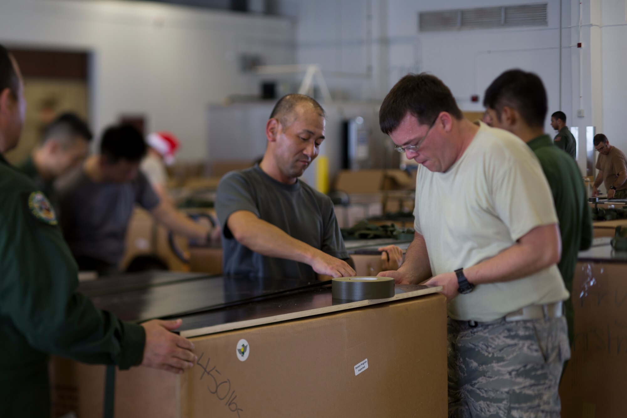 (Left to right) Japan Air Self-Defense Force Master Sgt. Atsushi Tanigawa, 3rd Tactical Airlift Wing, and U.S. Air Force Master Sgt. Zach Kirby, 36th Airlift Squadron flight engineer, build a low-cost, low-altitude bundle destined for the island of Fais, during Operation Christmas Drop at Andersen Air Force Base, Guam, Dec. 5, 2015. Operation Christmas Drop 2015 will be the first ever trilateral training event that includes additional air support from the Japan Air Self-Defense Force and Royal Australian Air Force. (U.S. Air Force photo by Osakabe Yasuo/Released)