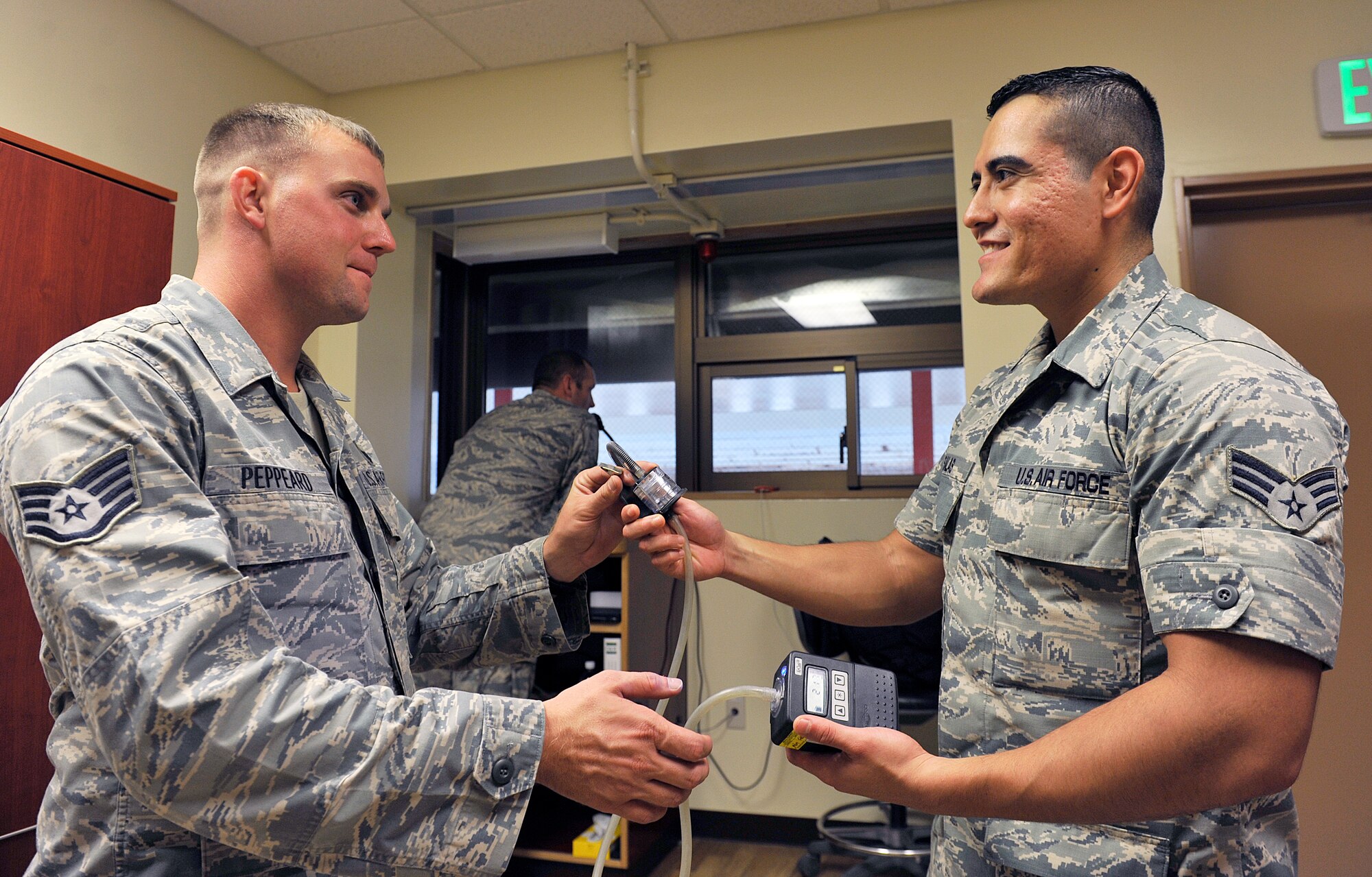 U.S. Air Force Staff Sgt. Jeffery Peppeard, 18th Security Forces Squadron combat arms instructor, receives an air sampling pump from Senior Airman Gerardo Salas, 18th Aerospace Medicine Squadron bioenvironmental engineering journeyman, at the combat arms training maintenance range, Dec. 3, 2015, at Kadena Air Base, Japan. The information collected from the air sampling pump provides key data to be used for assessing health risks from exposure to airborne contaminants in both occupational and environmental settings. (U.S. Air Force photo by Naoto Anazawa)