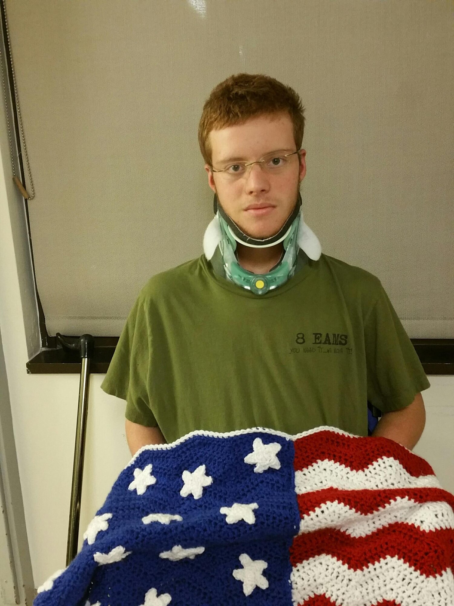 Gregory, son of Staff Sgt. Daniel Stein, 8th Expeditionary Air Mobility Squadron crew chief, stands holding a crochet flag while wearing his dad’s squadron T-shirt. In November, Gregory suffered a fractured C-1 vertebra when the all-terrain vehicle he was riding flipped over. After the accident he told his dad, “Dad you being there serving the country is my impetus to get up and walk.” Gregory is scheduled to be released Dec. 17th. . (U.S Air Force photo courtesy of Staff Sgt. Stein/Released)