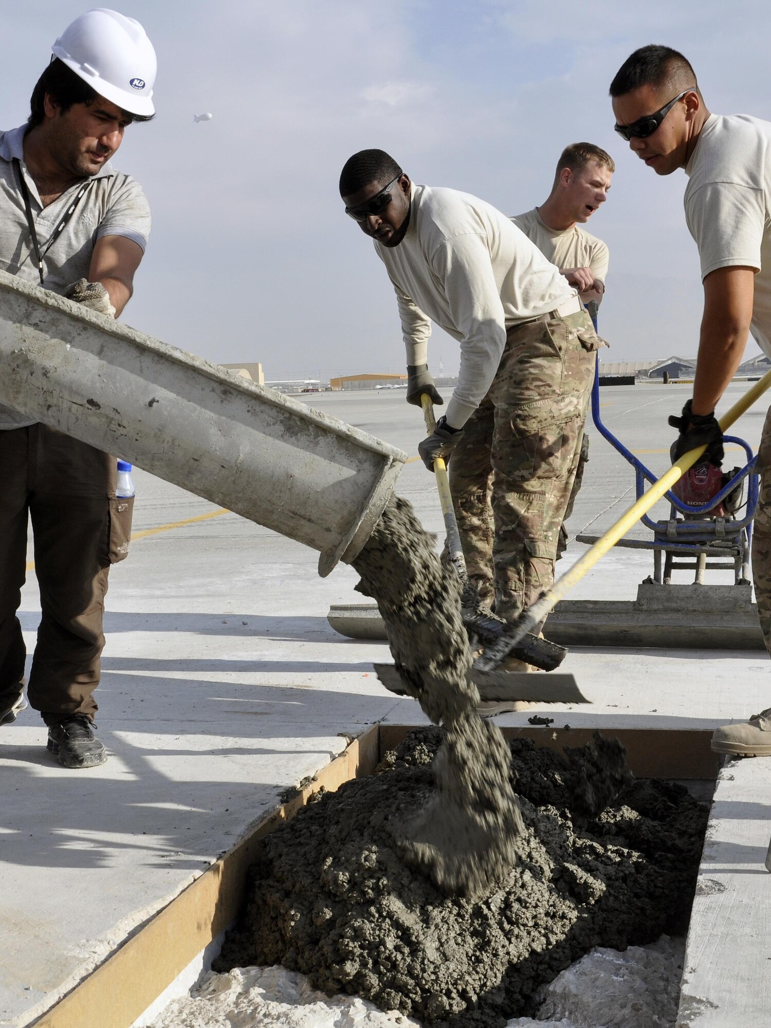 Staff Sgt. Richard Bonham, left, and Staff Sgt. Ranson Holt, both from the 455th Expeditionary Civil Engineer Squadron, scoop cement delivered by a contractor to repair a section of the flightline at Bagram Airfield, Afghanistan, Dec. 7, 2015. Airfield integrity concerns are reviewed twice a month by Airfield Management and 455th ECES. Once repairs are completed, these areas of the flightline should not require maintenance for up to 10 years.  (U.S. Air Force photo by Tech. Sgt. Nicholas Rau/Released)
