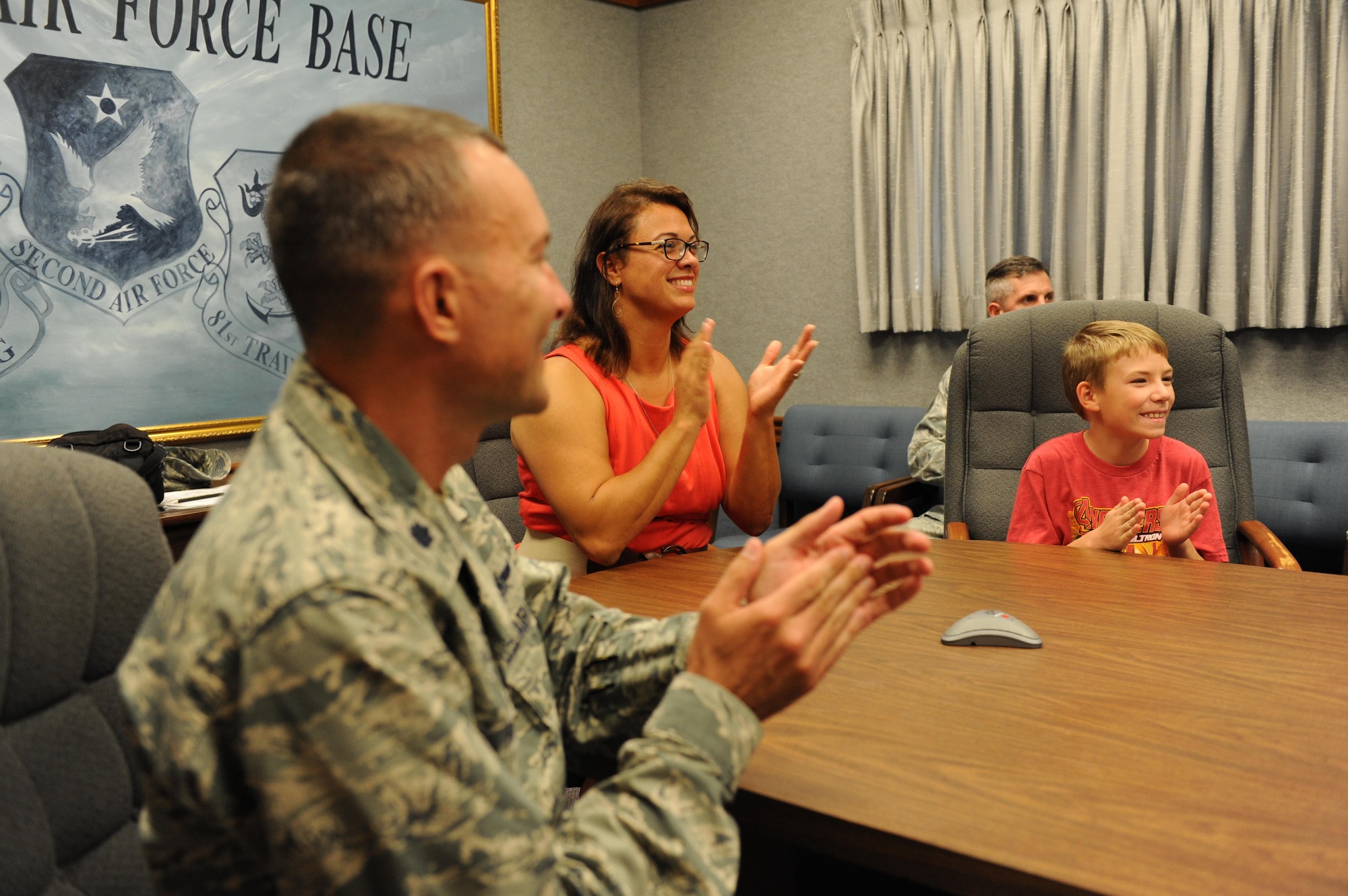 Lt. Col. Douglas Fowler, 338th Training Squadron commander, join Francesca Hendrickson and her son, Jackson, as they applaud after watching a video teleconference at Wall Studio as her husband, Tech. Sgt. Robert Hendrickson, 338th Training Squadron instructor, was promoted Nov. 30, 2015, Keesler Air Force Base, Miss. Hendrickson is currently deployed to Soto Cano Air Base, Honduras where he provides radio support for Joint Task Force-Bravo. (U.S. Air Force photo by Kemberly Groue)