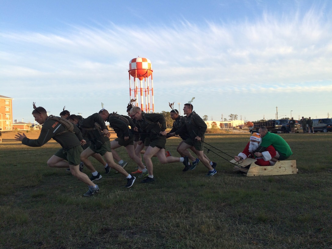 Combat Engineer Instruction Company Marines, wearing antlers; pull Lieutenant Colonel Taylor P. White, in a Santa suit; and First Sergeant Scott T. Braden, in an elf costume; across the parade field in a sleigh as part of the Marine Corps Engineer School Commanding Officer's Holiday Sleigh Relay Race at Courthouse Bay, Camp Lejeune, N.C. on Dec. 4, 2015. 