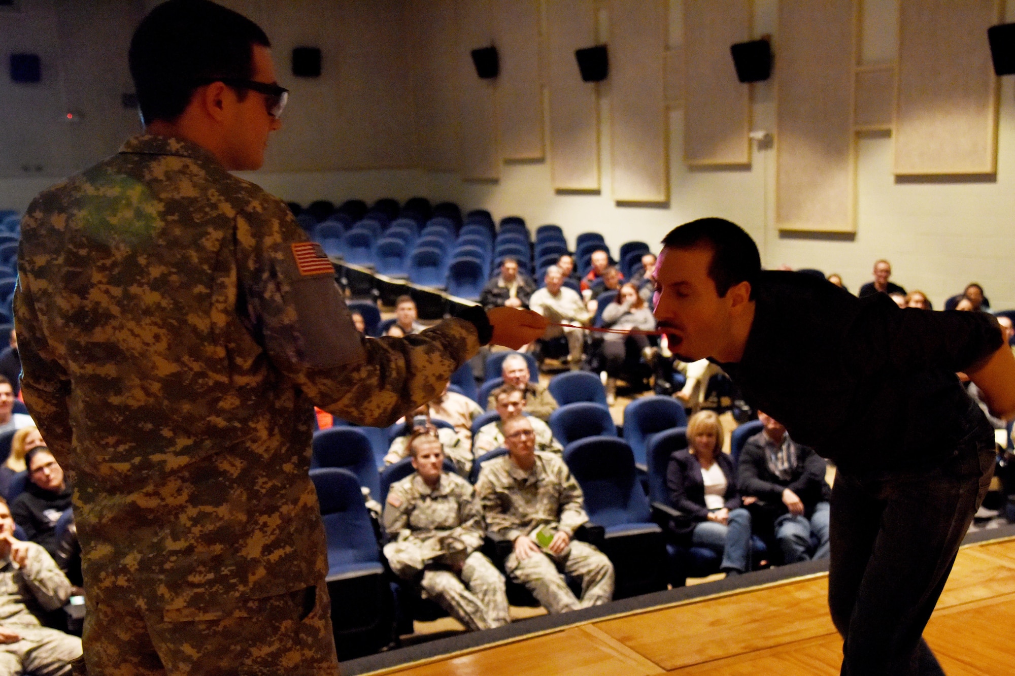 U.S. Army Pvt. Austin T. McCoy, 344th Military Intelligence Battalion student, pulls a metal hanger out the throat of Matt the Knife, magician and mentalist, during a magic show at the theater on Goodfellow Air Force Base, Texas, Dec. 4, 2015. After the show, Matt signed autographs, posed for photos and performed a few card tricks. (U.S. Air Force photo by Senior Airman Joshua Edwards/Released)