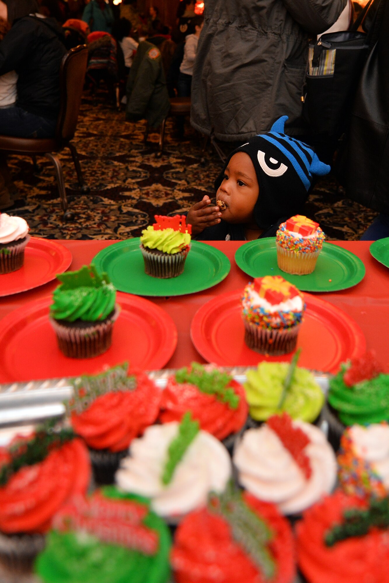 One-year-old Robert Young-Williams, son of U.S. Air Force Senior Airman Jaanna Young-Williams, finishes a cookie near the desserts table while at the annual Christmas Tree Lighting ceremony held at the Patriot Club on Dec. 3, Offutt Air Force Base, Neb.  Tables upon tables were lined with candy, cupcakes and gingerbread cookies with hot chocolate to wash it down.  In addition to the treats, the ceremony boasted a full dinner buffet for the hundreds of families in attendance.  (U.S. Air Force photo by Josh Plueger/Released)