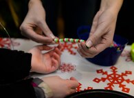 A volunteer helps a child with an arts and crafts project during a holiday tree and menorah lighting ceremony at Whiteman Air Force Base, Mo., Dec. 1, 2015. The 509th Force Support Squadron hosted the event that featured stations where children could decorate holiday cookies, take photos with Santa and enjoy live music. (U.S. Air Force photo by Sandra Marrero)