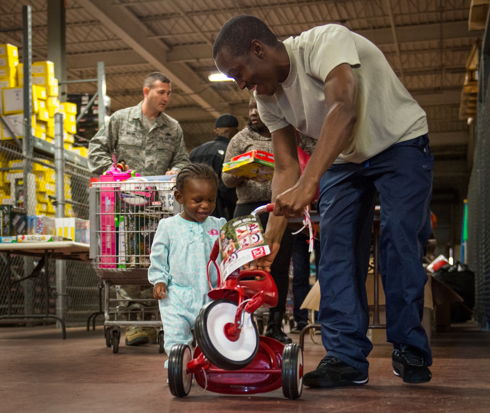 A family member helps his daughter push around her new tricycle she selected at the annual holiday toy distribution at Eglin Air Force Base, Fla., Dec. 4.  Approximately 2,000 toys were collected by donations made throughout the year. Toys, bikes, books, games, crafts, sports equipment and stuffed animals were given to active-military families in need of assistance during the holidays.  (U.S. Air Force photo/Samuel King Jr.)