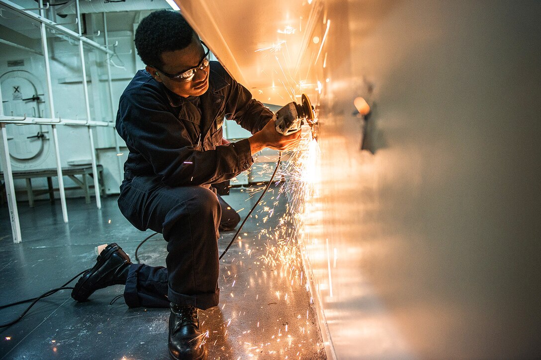U.S. Navy Seaman Leahmond Tyre uses a handheld grinder to smooth a bulkhead on the U.S. Navy's only forward-deployed aircraft carrier, the USS Ronald Reagan in Yokosuka, Japan, Dec. 8, 2015. The Ronald Reagan provides a combat-ready force that protects and defends the collective maritime interests of allies and partners in the Indo-Asia-Pacific region. U.S. Navy photo by Petty Officer 3rd Class James Lee