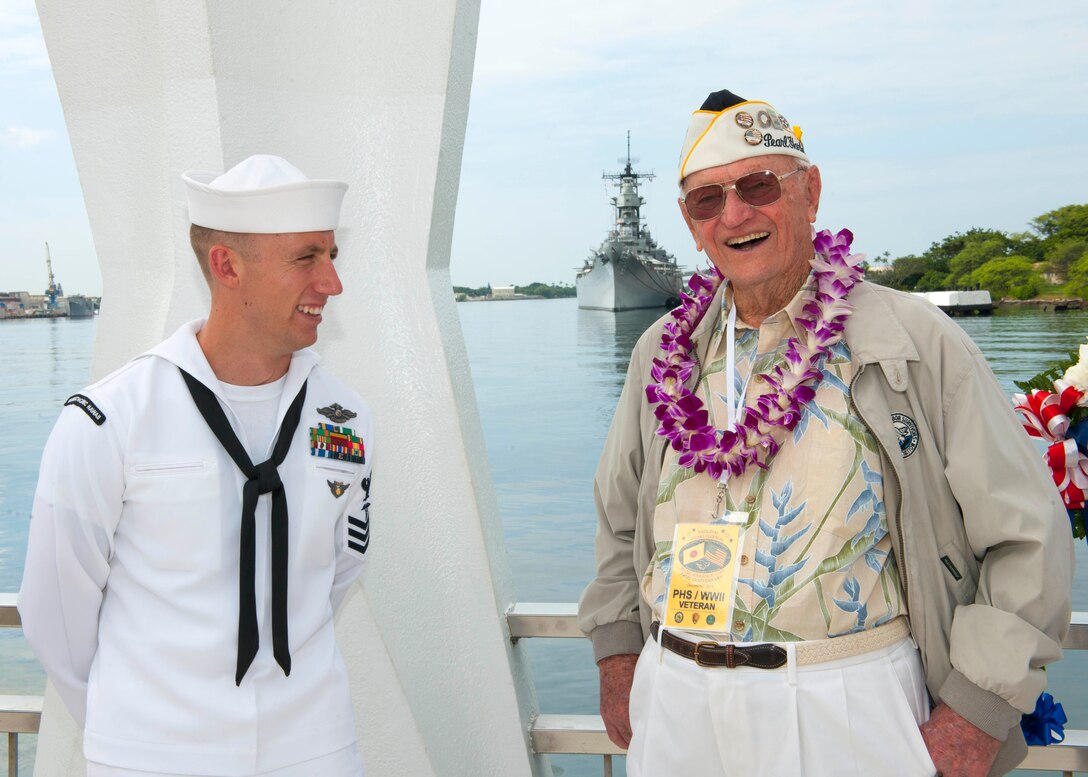 Ed Schuler, who survived the attacks on Pearl Harbor, Dec. 7, 1941, talks with a sailor during a wreath dedication ceremony in remembrance of the attacks 74 years ago, on Joint Base Pearl Harbor-Hickam, Hawaii, Dec. 7, 2015. U.S. Navy photo by Petty Officer 2nd Class Jeff Troutman