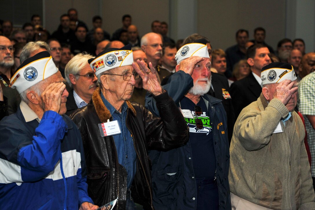 Pearl Harbor survivors salute as the color guard presents the colors in the Naval Undersea Museum Jack Murdock Auditorium during the annual Naval Undersea Warfare Center Division Keyport Pearl Harbor Remembrance ceremony in Keyport, Wash., Dec. 7, 2015. U.S. Navy photo by Petty Officer 3rd Class Charles D. Gaddis IV