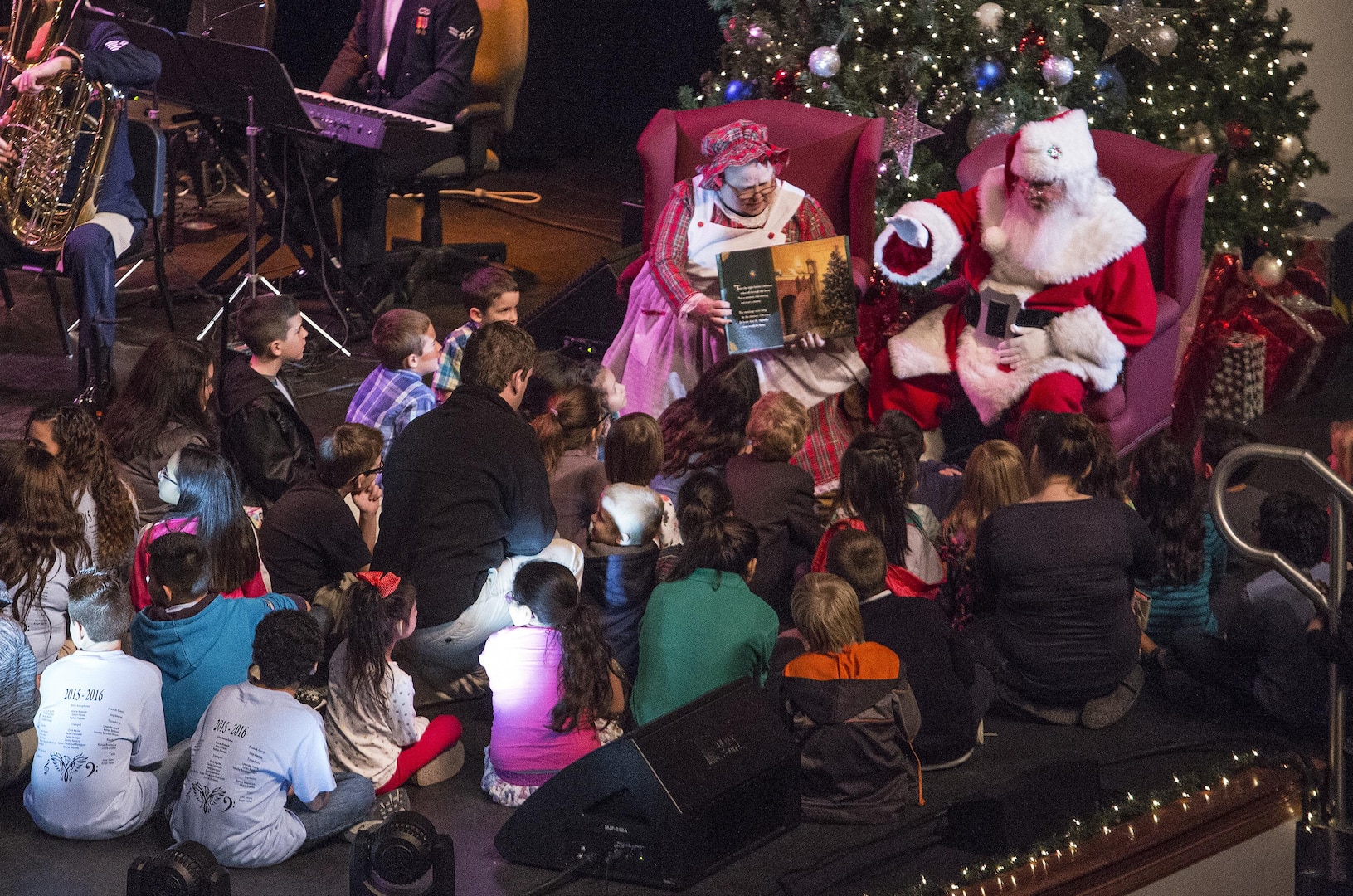 Santa and Mrs. Clause display a childrens book while United States Air Force Band of the West perform holiday music during the Holiday in Blue concert Dec. 7, 2015 at the Edgewood Independent School District Theatre for the Performing Arts in San Antonio, Texas. The concert included a variety of holiday songs from around the world, a children’s story and a sing-a-long. Attendees included members of JBSA, community members and retirees. The Airmen assigned to the band are highly-trained professional musicians who have dedicated themselves to serving their country through music. (U.S. Air Force photo by Johnny Saldivar)