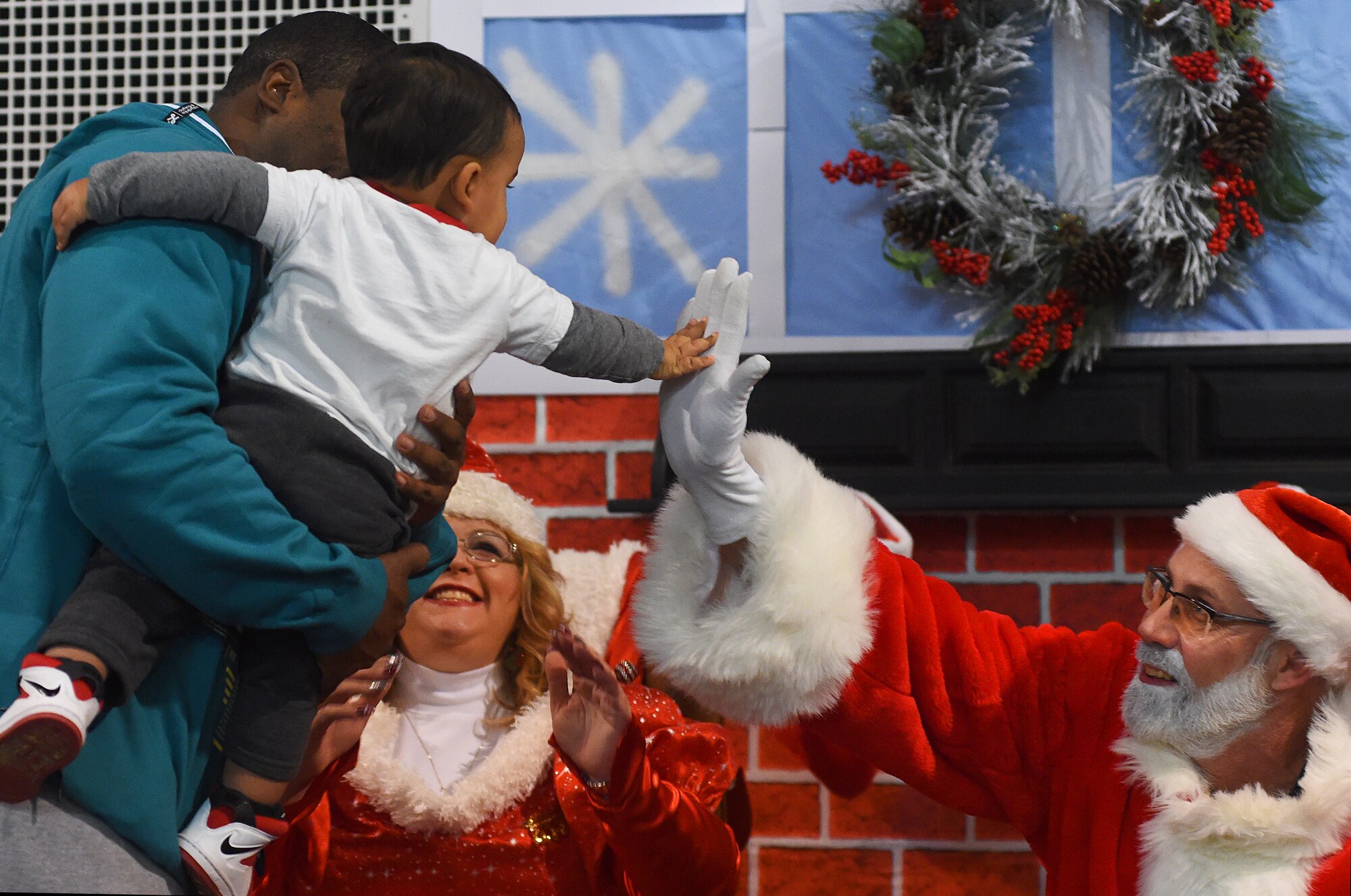 Solomon Gray, 1, son of Tech Sgts. Amy Gray, 90th Force Support Squadron, and Brandon Gray, 90th Civil Engineer Squadron, gives Santa Claus a high-five as Mrs. Claus looks on in the Fall Hall Community Center on F.E. Warren Air Force Base, Wyo. Dec. 4, 2015. The Grays were attending the base's annual tree lighting ceremony. (U.S. Air Force photo by R.J. Oriez)