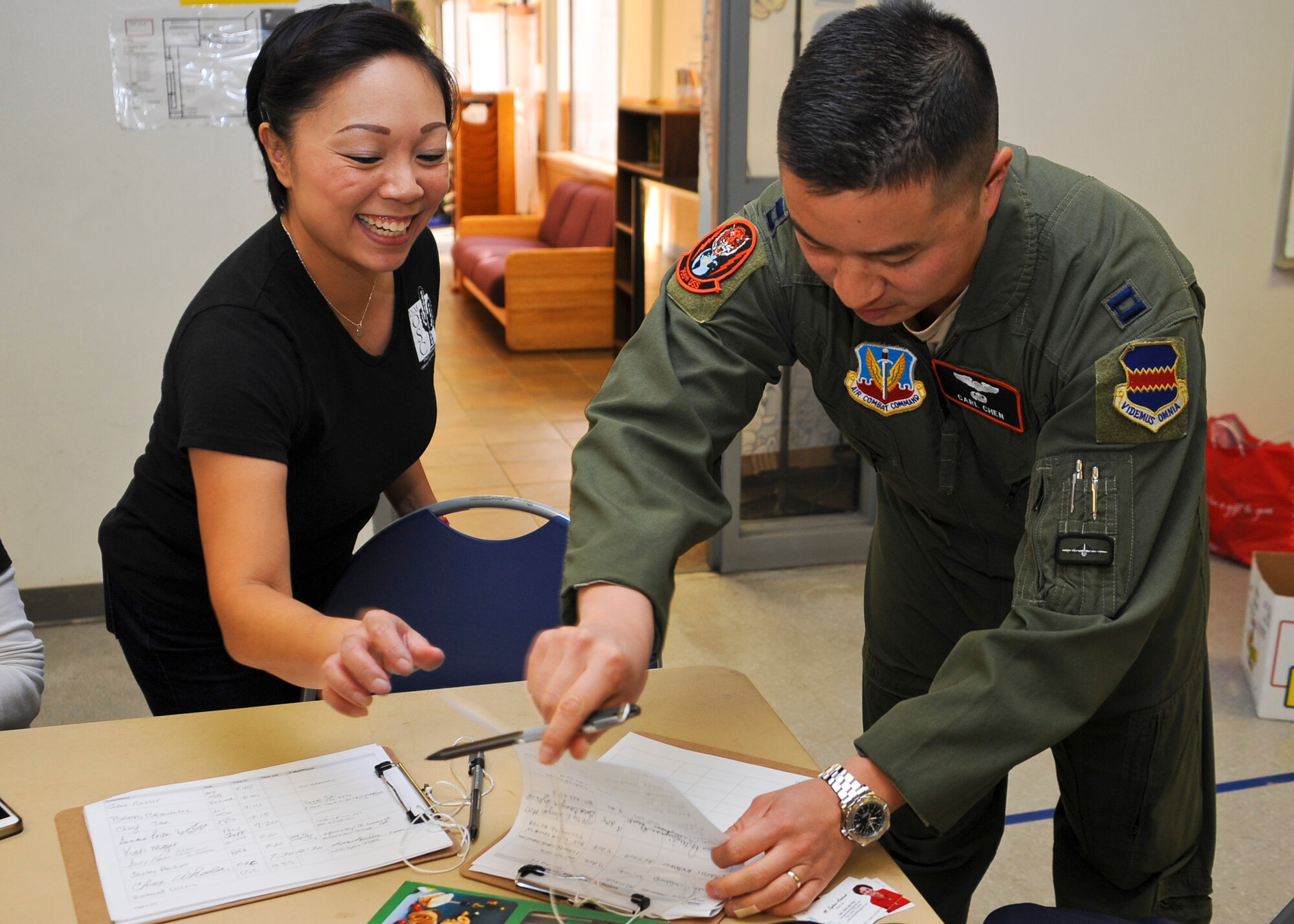Vivian Vralsted, Cookie Crunch chairwomen and wife of U.S. Air Force Capt. Bryan Vralsted, 355th Medical Operations Squadron mental health flight commander, directs Capt. Carl Chen, 755th Operational Support Squadron assistant director of operations, to sign in on the Cookie Crunch donation sheet at Davis-Monthan Air Force Base, Ariz., Dec. 7, 2015. D-M AFB’s annual Cookie Crunch distributed donated cookies to approximately 700 Airmen who reside in the base dorms during the holiday season. (U.S. Air Force photo by Airman 1st Class Ashley N. Steffen/Released) 