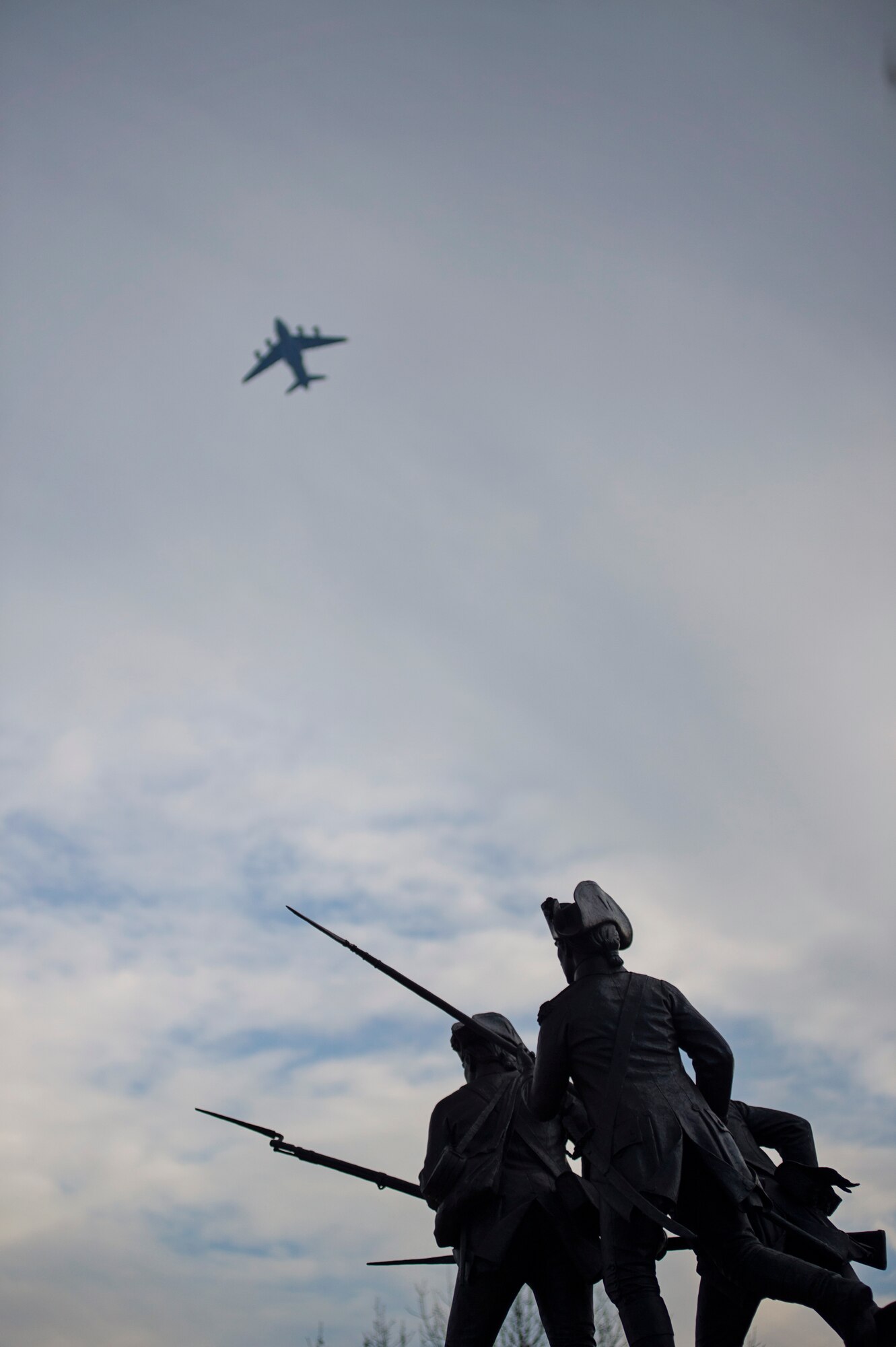 A Team Dover C-17A Globemaster III flies above after takeoff with the Delaware Continentals memorial in the foreground, taken December 7, 2015, in downtown Dover, Del. Dec 7 marks the anniversary of the Pearl Harbor attacks and also Delaware Day, a state holiday to recognize the state being the first to ratify the Federal Constitution in 1787. (U.S. Air Force photo/Capt. Bernie Kale)