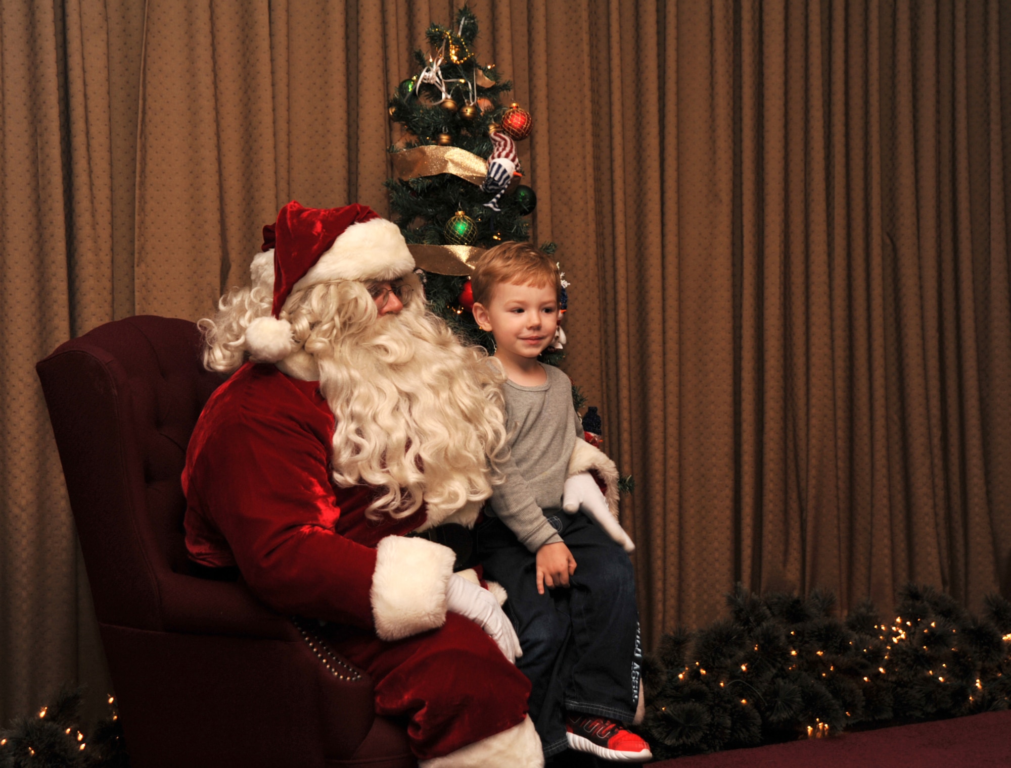 Jace Economides, 4, sits on Santa’s lap at the Holiday Tree Lighting ceremony on Grand Forks Air Force Base, North Dakota, Dec. 7, 2015. Santa arrived at the club escorted by the Grand Forks AFB Fire Department on a fire truck and stayed to listen to children’s Christmas wishes. (U.S. Air Force photo by Senior Airman Bonnie Grantham/released)