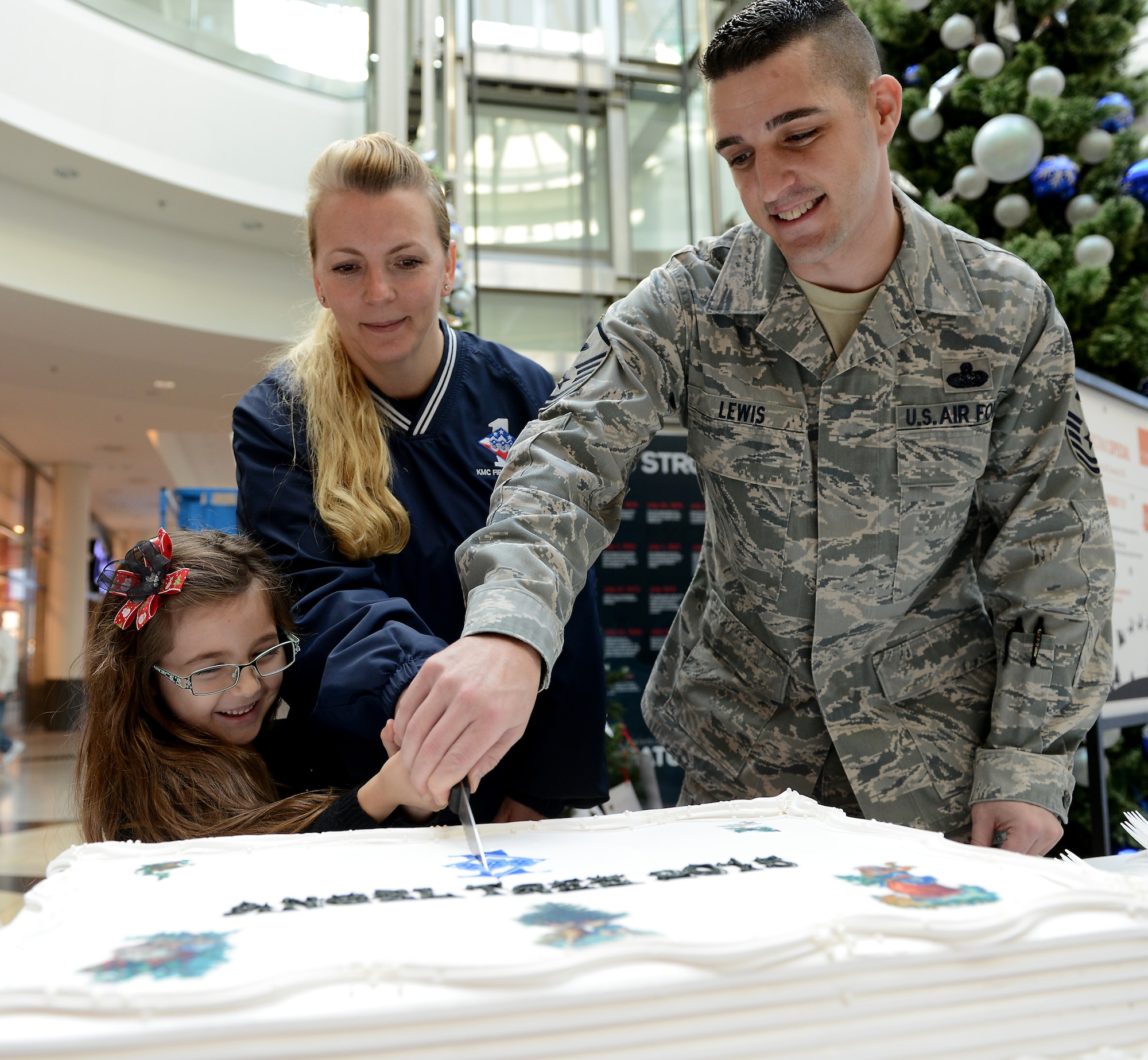 Caylee Lewis cuts a cake with her father, Master Sgt. Allen Lewis, 450th Intelligence Squadron first sergeant, and Master Sgt. Kimberly Dixon, 86th Aeromedical Evacuation Squadron first sergeant, during the Angel Tree 2015 program kickoff Dec. 7, 2015, at Ramstein Air Base, Germany. Run by the Kaiserslautern Military Community First Sergeant Council, Angel Tree is an annual outreach program whose goal is to provide assistance to Airmen and their families during the holiday season and throughout the year. (U.S. Air Force photo/Staff Sgt. Timothy Moore)