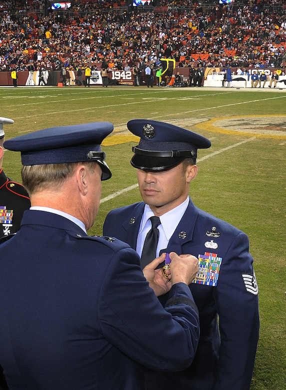 Technical Sgt. Christopher Ferrell, 11th Civil Engineer Squadron's Explosive Ordnance Disposal flight, is honored for his Purple Heart Medal by Maj. Gen. Darryl Burke, Air Force District of Washington commander, during an NFL half-time show of the Washington Redskins versus Dallas Cowboys game, Dec. 7, 2015. Ferrell was wounded while disarming a road-side bomb in Afghanistan in 2009. The ceremony was part of the Washington Redskins’ annual Salute to Service game which honors the nation's veterans and active duty military. (U.S. Air Force photo by James E. Lotz/RELEASED).