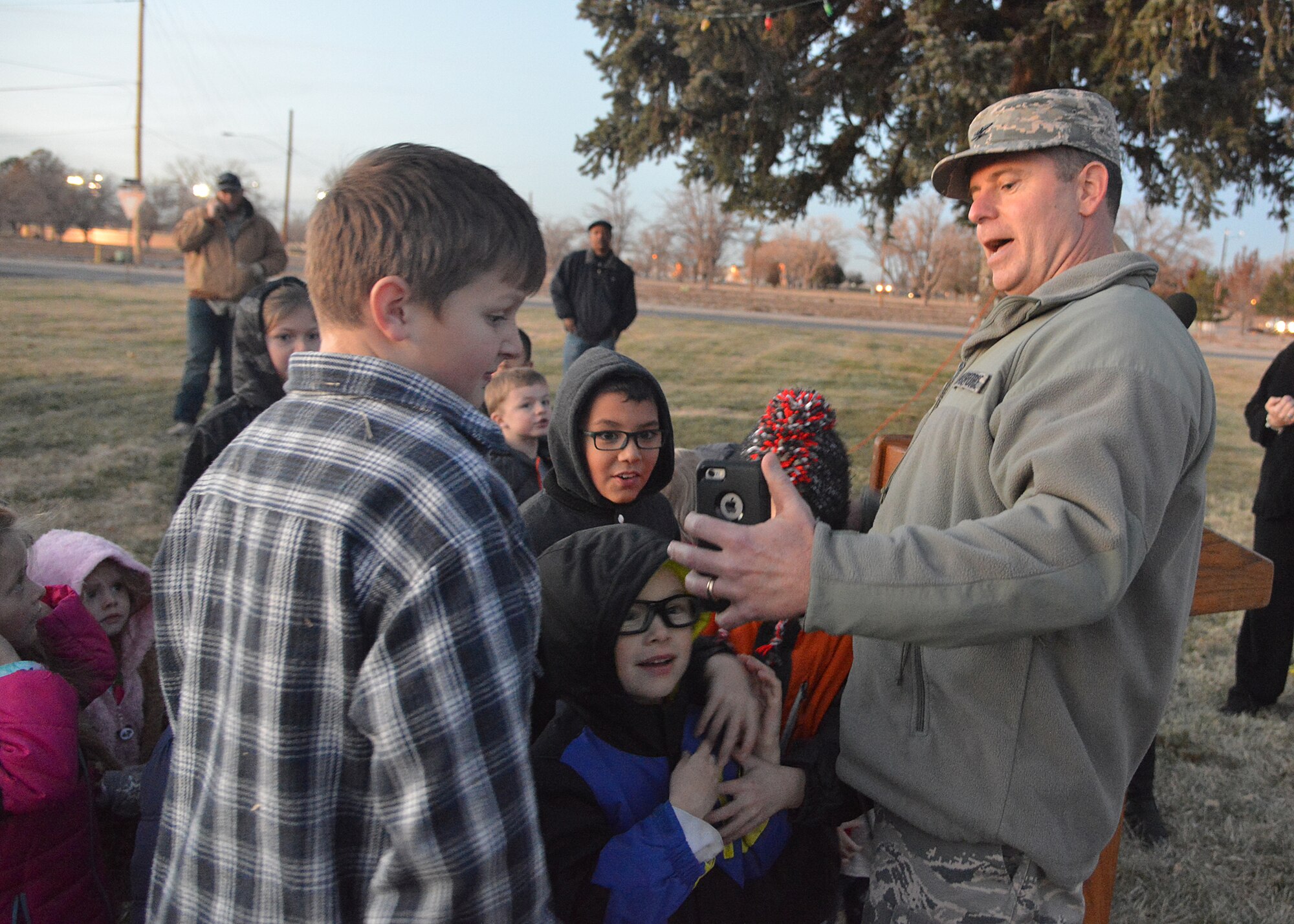 Col. Eric Froehlich, 377th Air Base Wing commander, shows children an app on his phone that allows him to activate the tree lights at the annual tree lighting at the Base Chapel Annex Dec. 3. Team Kirtland members gathered for the tree lighting, followed by Santa visits, caroling, arts and crafts and refreshments. (Photo by Todd Berenger)