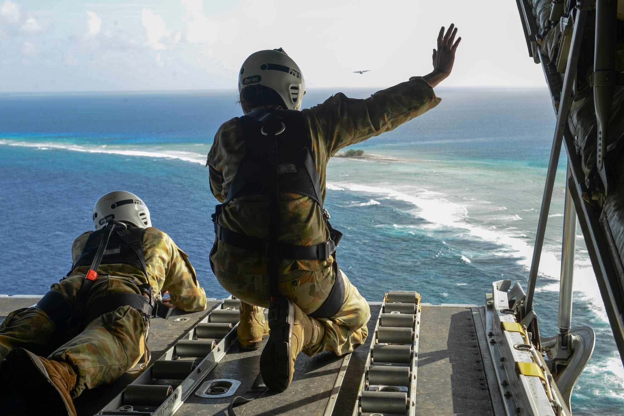 Australian Army Cpl. Teome Matamua and Sgt. Phillip McIllvaney, 176th Air Dispatch Squadron loadmasters, wave to islanders in the Federated States of Micronesia from the back of a C-130J Super Hercules after delivering donated goods and critical supplies to the islanders Dec. 8, 2015, during Operation Christmas Drop. The 2015 Christmas Drop missions marked the first time the event included trilateral air support from the Japan Air Self-Defense Force and RAAF. (U.S. Air Force photo/Staff Sgt. Katrina Brisbin)
