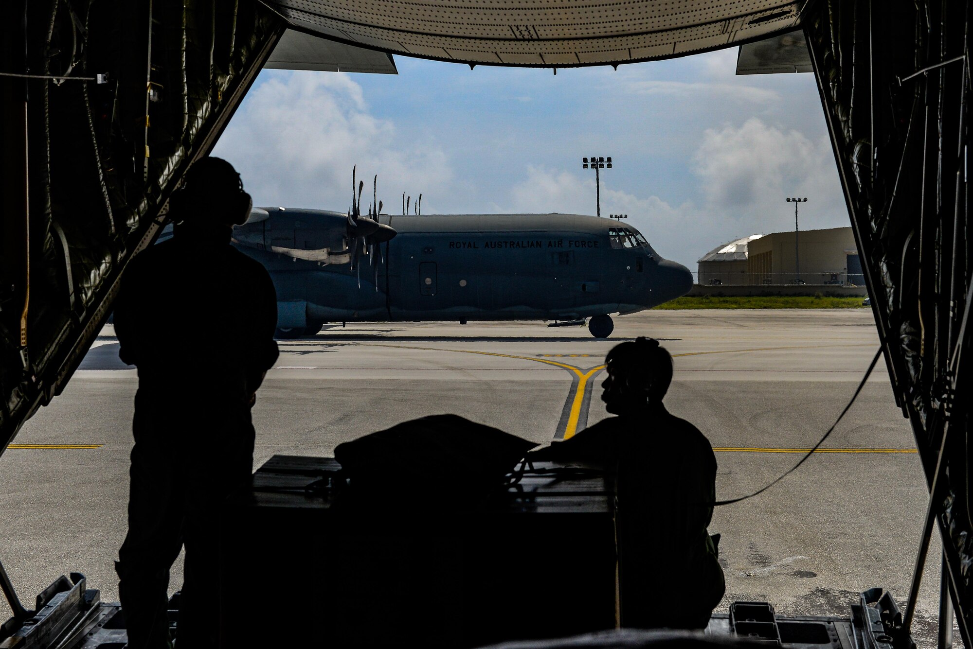 Japanese Master Sgt. Toyonaga Toshihisa, left, and Tech. Sgt. Takahashi Tetsuki, both loadmasters with the Japanese Air Self-Defense Force 1st Tactical Airlift Wing, watch as a Royal Australian Air Force C-130J Hercules taxis along the flightline Dec. 8, 2015, at Andersen Air Force Base, Guam. The 64th year of Christmas Drop, which began in 1952, marked the first time international aviators from Japan and Australia joined the humanitarian airdrop mission. (U.S. Air Force photo/Staff Sgt. Alexander W. Riedel)