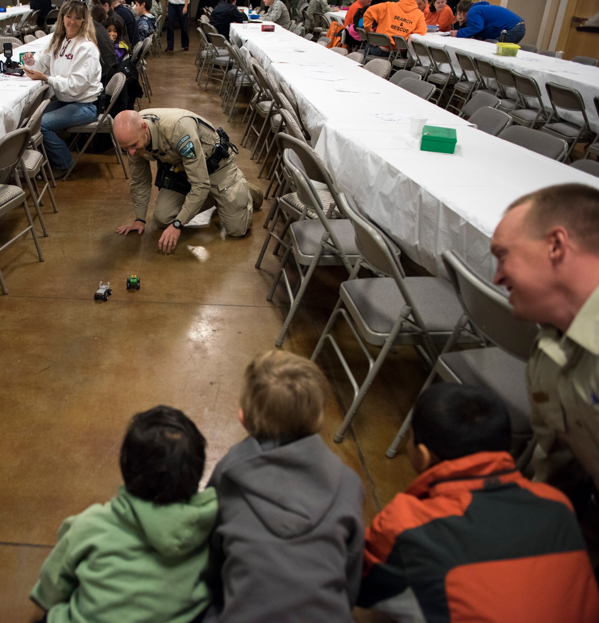 Local law enforcement race cars back and forth during the Shop with a Cop event, Dec. 5, 2015, at the Mountain Home, Idaho Elk Lodge. Officers encouraged the children by being the first to join in the festivities. (U.S. Air Force photo by Airman 1st Class Connor J. Marth/Released)