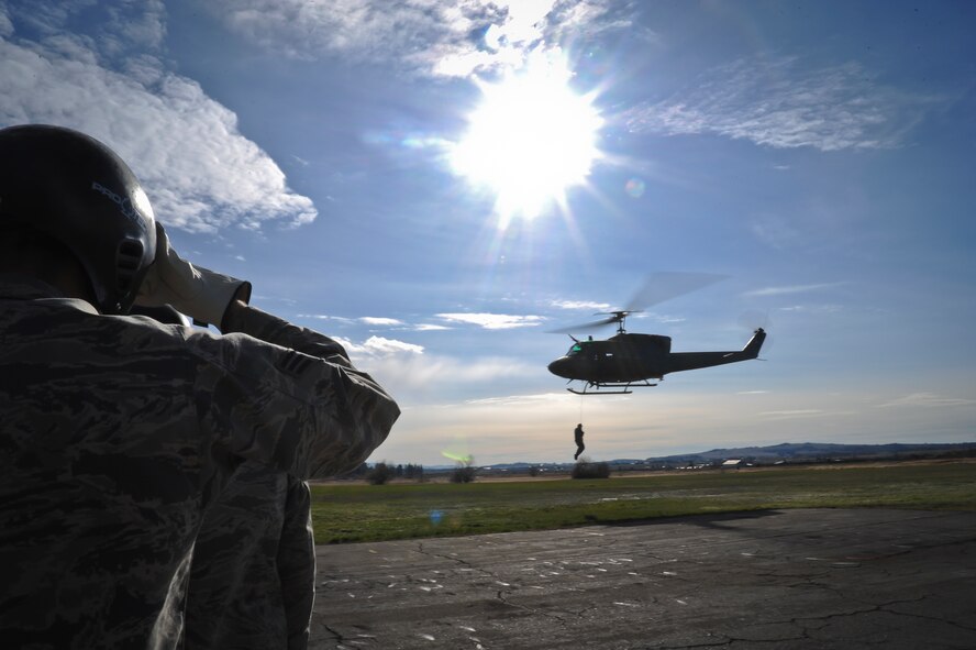 A combat survival training student observes as another student is hoisted into the UH-1N Iroquois helicopter, April 8, 2015, at Fairchild Air Force Base, Wash. Students learn a multitude of skills while attending the Survival School, to include: hoist training, vectoring a helicopter and compass reading. (U.S. Air Force photo/Airman 1st Class Nick J. Daniello)
