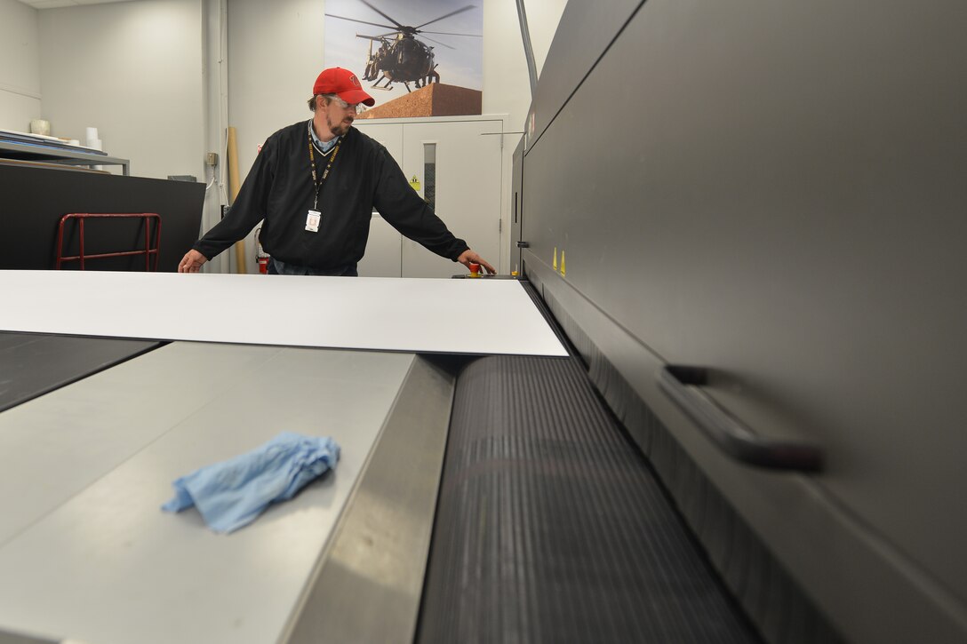 Ken Clevenger, a graphic service specialist with the Joint Base Langley-Eustis Enterprise Multimedia Center, leads poster board into an ultraviolet printer at Fort Eustis, Va., Dec. 1, 2015. The center is capable of printing targets as well as life-size prints for various training, morale and support projects. (U.S. Air Force photo by Staff Sgt. Natasha Stannard)