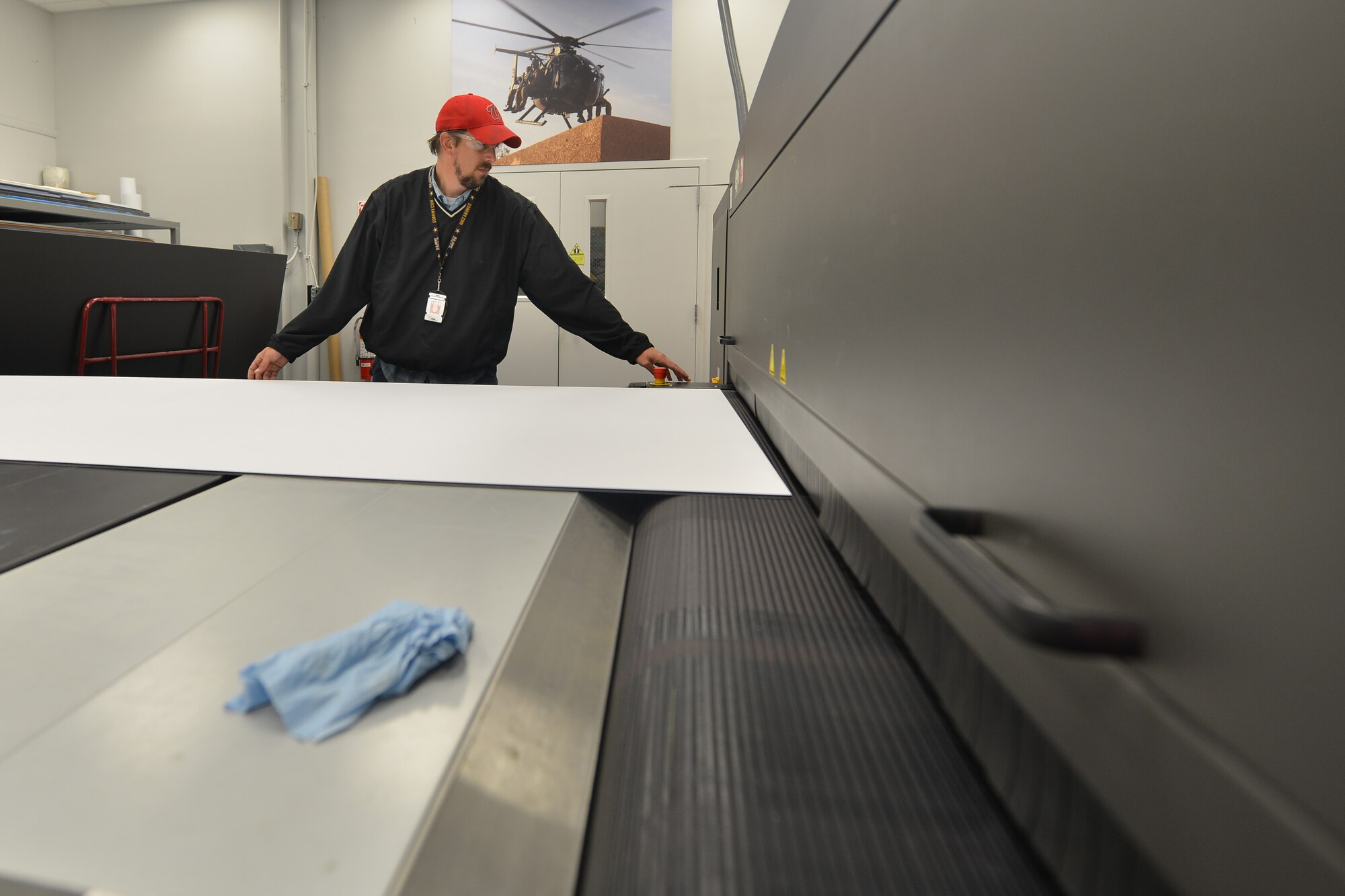 Ken Clevenger, a graphic service specialist with the Joint Base Langley-Eustis Enterprise Multimedia Center, leads poster board into an ultraviolet printer at Fort Eustis, Va., Dec. 1, 2015. The center is capable of printing targets as well as life-size prints for various training, morale and support projects. (U.S. Air Force photo by Staff Sgt. Natasha Stannard)