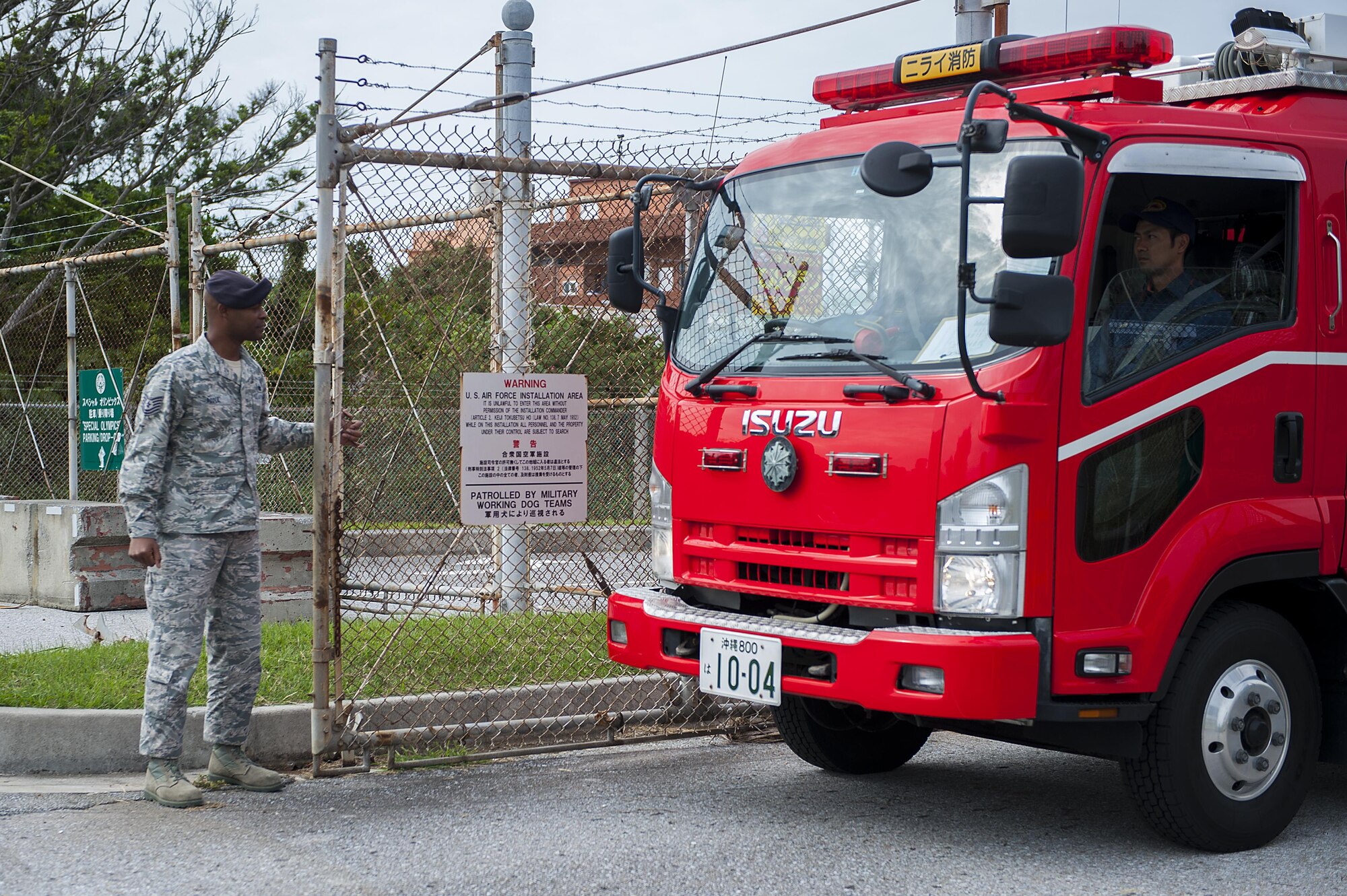U.S. Air Force Tech Sgt. Teddy Poole, 18th Security Forces Squadron police service NCO in charge, opens a gate for a Nirai Fire Department vehicle during an exercise Dec. 3, 2015, at Kadena Air Base Japan. Base entry was provided for first responders who may need to use base roads in the instance of a flooding that blocks off other routes. (U. S. Air Force photo by Airman 1st Class Corey M. Pettis/Released)