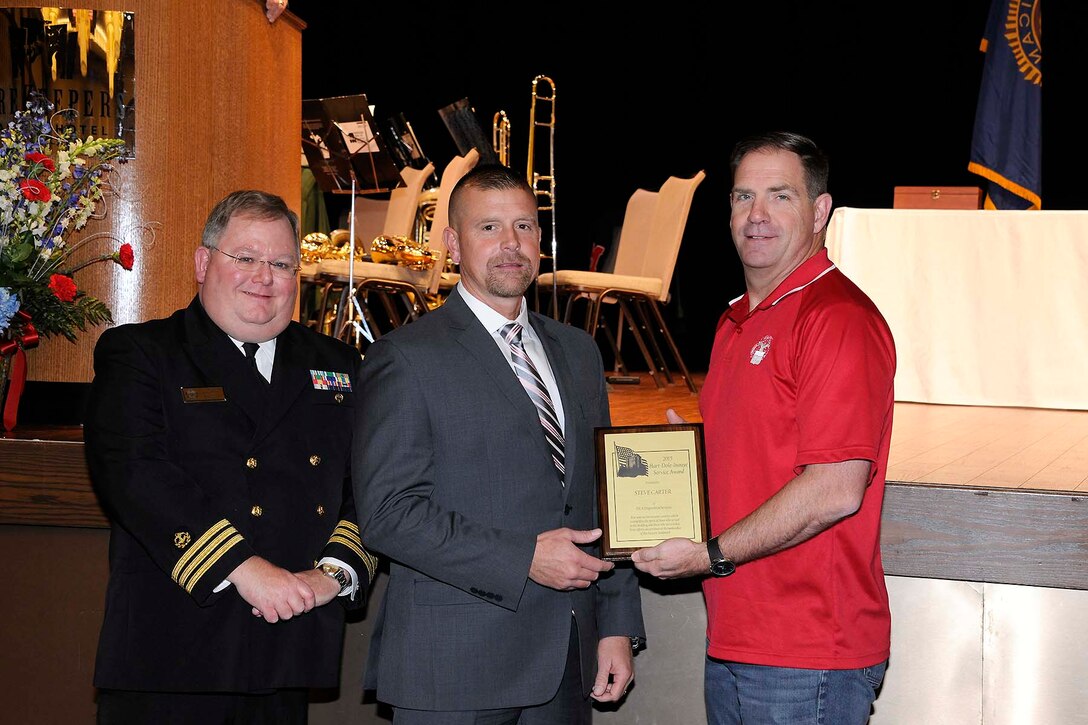 Steve Carter (center) receives the Hart-Dole-Inouye Federal Center Service Award from DLA Disposition Services Director Mike Cannon (right) and Retired Navy Cmdr. T.R. Shaw for demonstrating the “spirit of service” synonymous with the center and its namesakes.