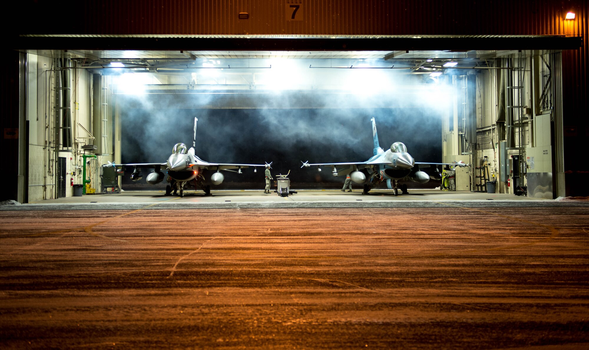 Exhaust billows as two F-16 Fighting Falcon fighter aircraft engines start in Dock 7 at Eielson Air Force Base, Alaska, Dec. 7, 2015. More than 30 maintenance Airmen worked an early shift to help launch several jets to Tyndall Air Force Base, Florida, for CHECKERED FLAG 16-1, a large-force exercise that simulates a large number of aircraft in a deployed environment to cross-check weapons systems. (U.S. Air Force photo by Staff Sgt. Shawn Nickel/Released)