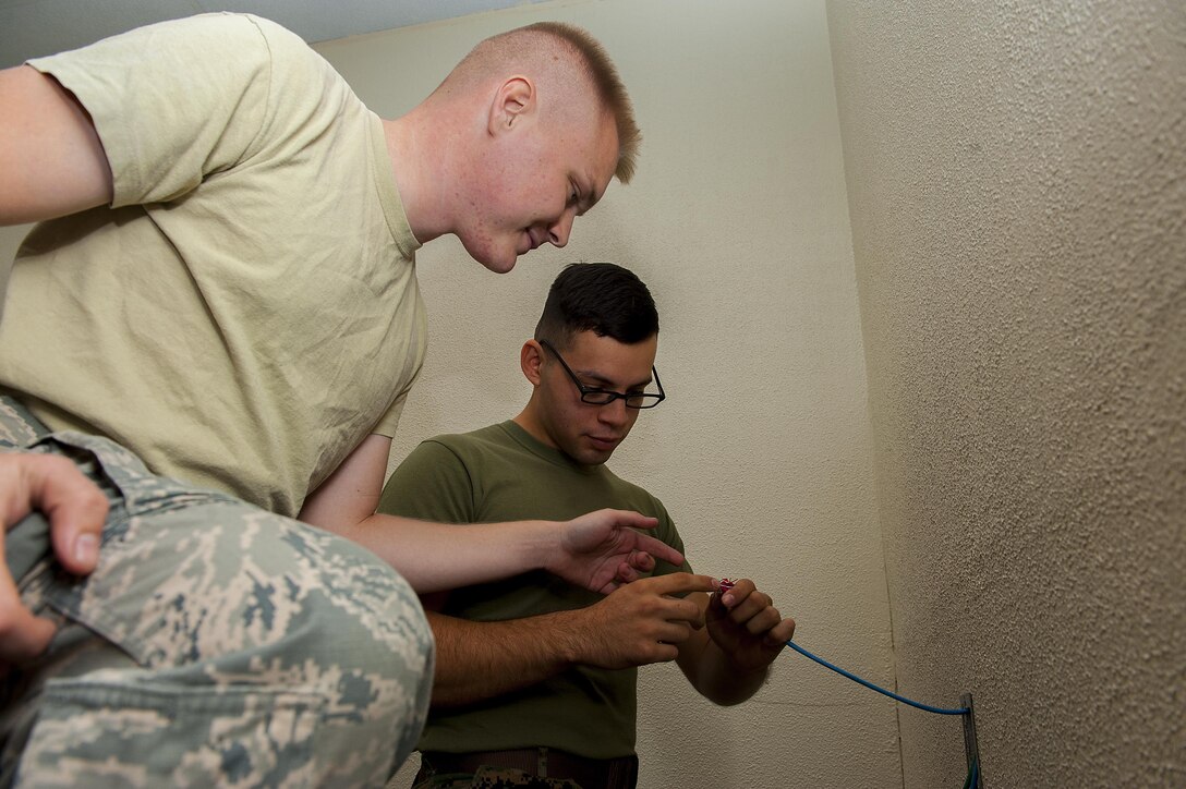 U.S. Marine Corps Cpl. Benjamin Trujillo, a construction wireman with Headquarters and Service Battalion, G-6 Division, Telephone Systems Branch, and Air Force Senior Airman Jacob Schroader, 18th Communications Squadron cable and antenna systems journeyman, work together to install telephone wiring Dec. 9, 2015, at Kadena Air Base, Japan. The 18th CS received two Marines from Camp Foster to participate in an exchange program to help both Airmen and Marines use partnership in joint operations. (U.S. Air Force photo by Airman 1st Class Corey M. Pettis)