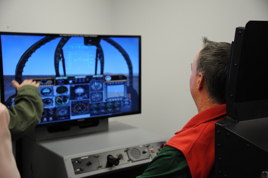U.S. Air Force Capt. Kimberly Dowd, 355th Aerospace Medical Squadron human performance flight commander, shows Chris Edwards, 355th Operations Group honorary commander and owner of Tucson Appliance, how a static flight simulator operates at Davis-Monthan Air Force Base, Ariz., Dec. 2, 2015. With an attachment above  the simulator allows pilots to experience reduced oxygen induces hypoxia without the dangers of flying. (U.S. Air Force photo by Airman 1st Class Ashley N. Steffen/Released)