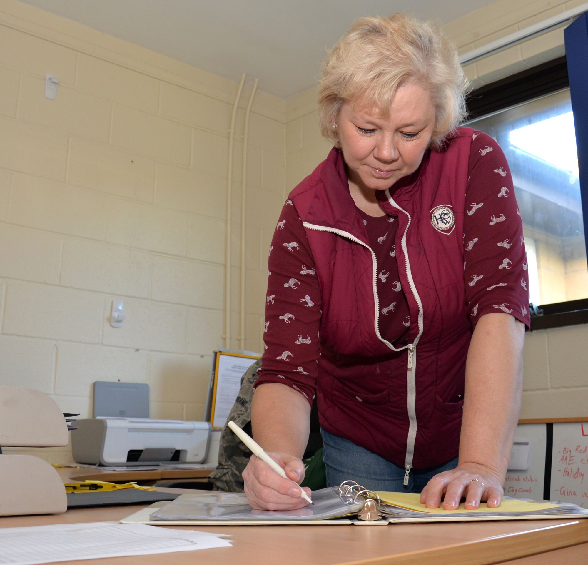 Deborah Black, 100th Security Forces Squadron kennel attendant, checks a binder for outstanding work orders Dec. 4, 2015, on RAF Mildenhall, England. As well as taking care of the dogs, Black keeps the military working dog facility tidy and clean, answers telephones and is one of the building custodians. (U.S. Air Force photo by Gina Randall/Released)