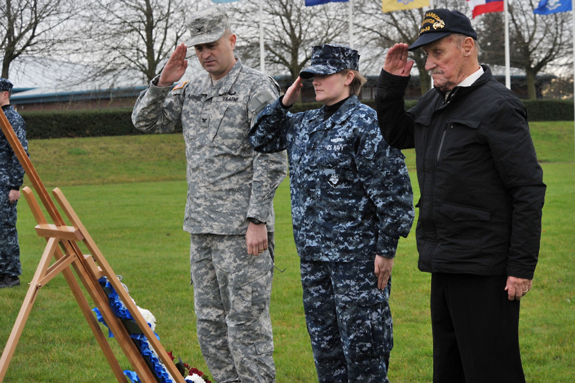 From left, U.S. Army Col. Mark Kjorness, U.S. Africa Command joint intelligence director, Navy Seaman Sydney, USAFRICOM division analyst, and Pearl Harbor survivor, former Marine Sgt. John Egan salute a wreath after placing it to honor Pearl Harbor casualties during the 74th Pearl Harbor Commemoration Ceremony at RAF Molesworth, United Kingdom, Dec. 7, 2015. In addition to the wreath laying, the ceremony included the playing of taps, a three-volley salute by the 423rd Honor Guard and an aerial flyby performed by the 48th Fighter Wing F-15 Eagle pilots. (U.S. Air Force photo by Staff Sgt. Ashley Tyler/Released) (Last name removed for security purposes)