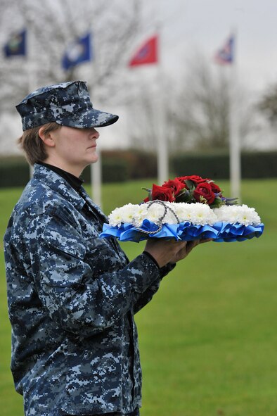 U.S. Navy Seaman Sydney, U.S. Africa Command division analyst, holds a wreath designed as an anchor to honor the fallen heroes of Pearl Harbor during the 74th Pearl Harbor Commemoration Ceremony at RAF Molesworth, United Kingdom, Dec. 7, 2015. Pearl Harbor survivor, former Marine Sgt. John Egan and U.S. Army Col. Mark Kjorness, USAFRICOM joint intelligence director, joined Sydney in saluting the wreath after it was placed. (U.S. Air Force photo by Staff Sgt. Ashley Tyler/Released)(Last name removed for security purposes)