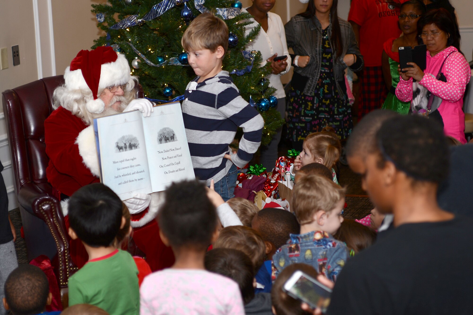 Santa Claus and his helper Joshua Saine, child of U.S. Army Col. Sam Saine, U.S. Army Central 4th Battlefield Coordination Detachment commander,  read a story to Team Shaw children at the Carolina Skies Club and Conference Center at Shaw Air Force Base, S.C., Dec. 12, 2015. Santa read “’Twas the Night Before Christmas” to the children as part of the 20th Force Support Squadron’s “Breakfast with Santa in your Pajamas” event, during which Santa also gave out gifts to children in attendance. (U.S. Air Force photo by Senior Airman Zade Vadnais)
