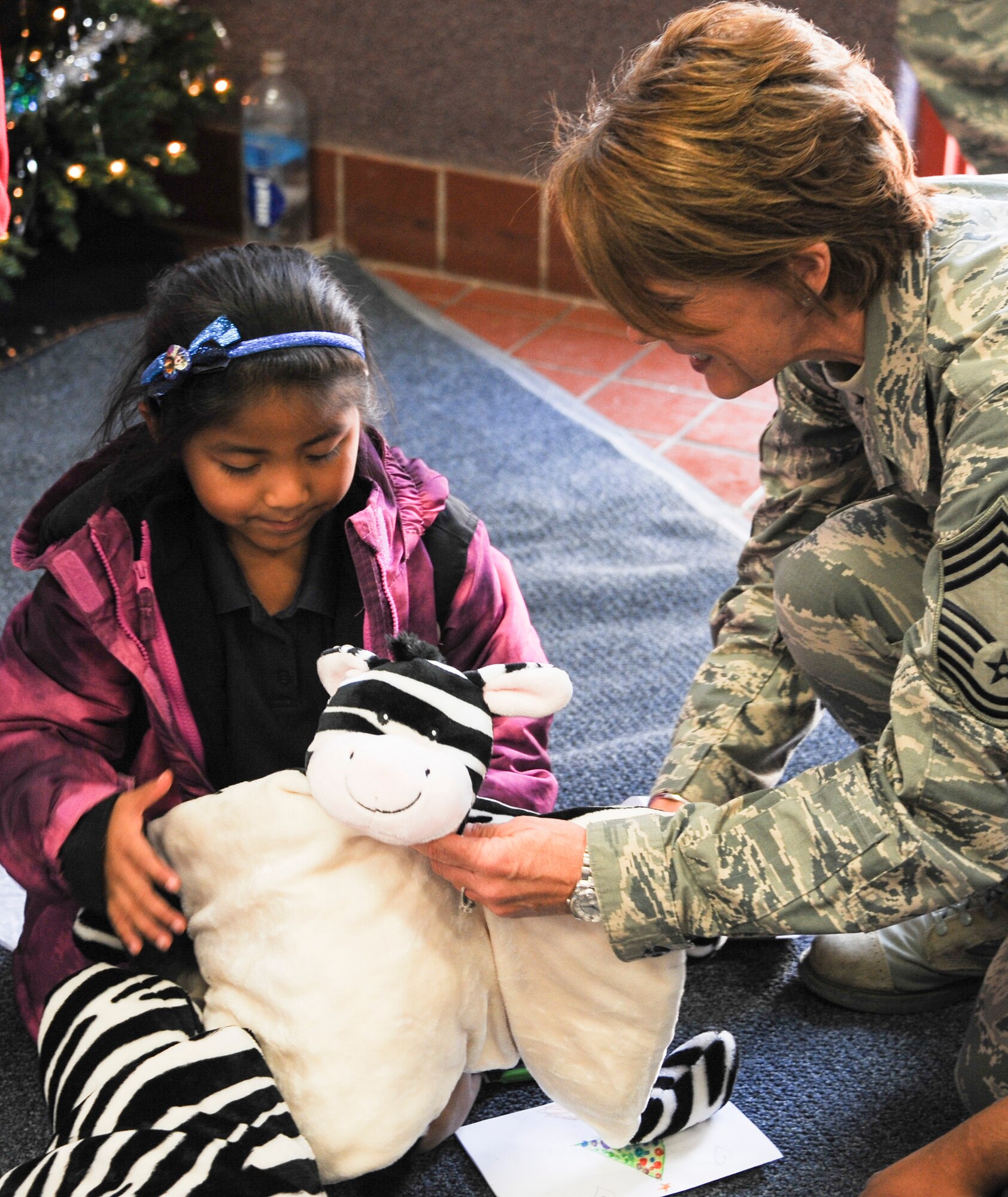 U.S. Air Force Chief Master Sgt. Dawn Kolczynski, 355th Medical Group superintendent, helps a San Xavier Mission School student unwraps a present during Davis-Monthan Air Force Base’s 50th Anniversary Santas in Blue event in Tucson, Ariz., Dec. 10, 2015. San Xavier Mission School is an Native American reservation, Catholic private school in southern Tucson that originated in the neighboring mission in 1865. (U.S. Air Force photo by Airman 1st Class Ashley N. Steffen/Released)
  
