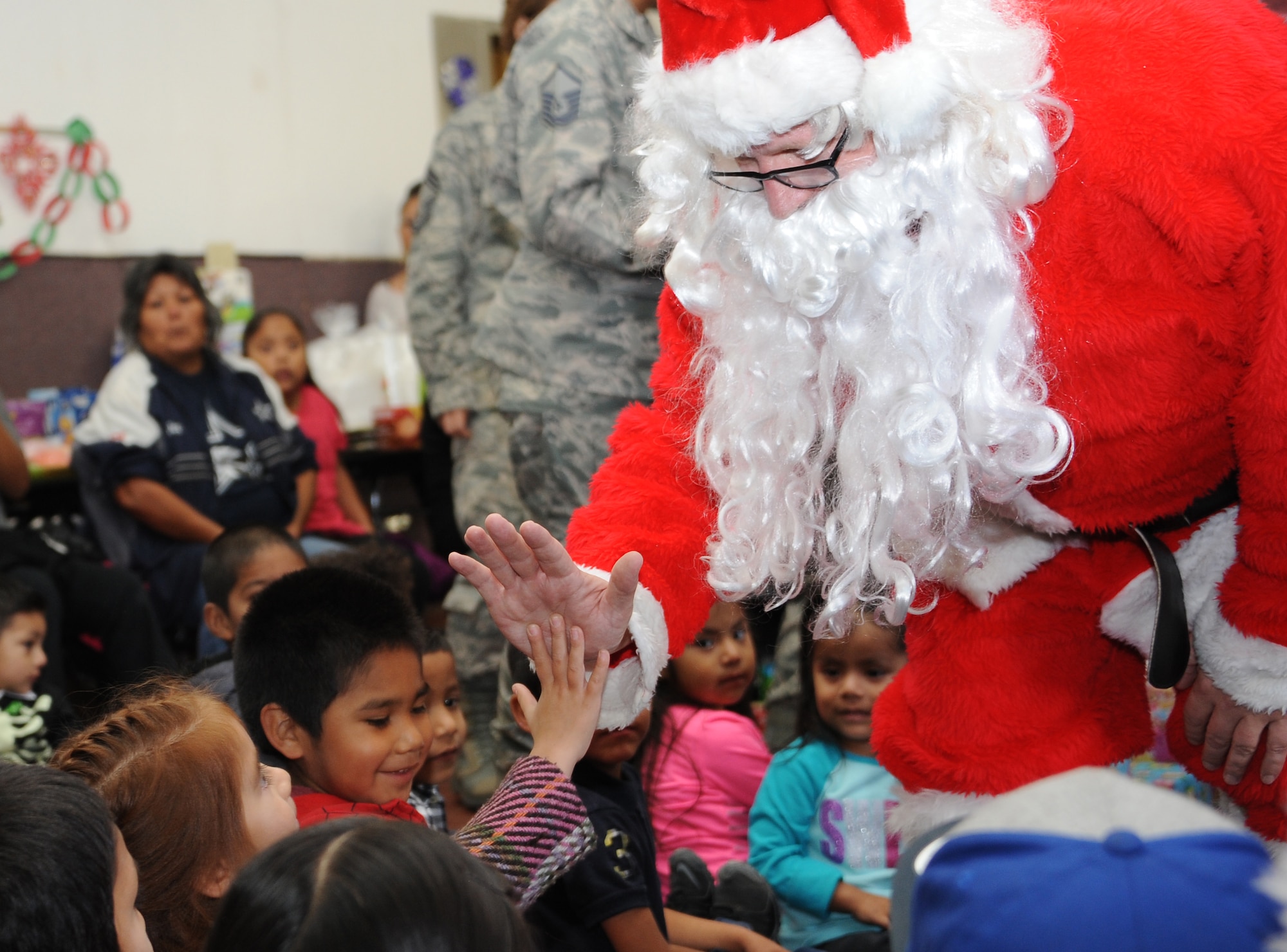 Santa gives high-fives and greets San Xavier Mission School students during Davis-Monthan Air Force Base’s 50th Anniversary Santas in Blue event in Tucson, Ariz., Dec. 10, 2015. Student’s families brought lunch for D-M AFB volunteers and watched their children unwrap gifts and meet Santa Claus. (U.S. Air Force photo by Airman 1st Class Ashley N. Steffen/Released)